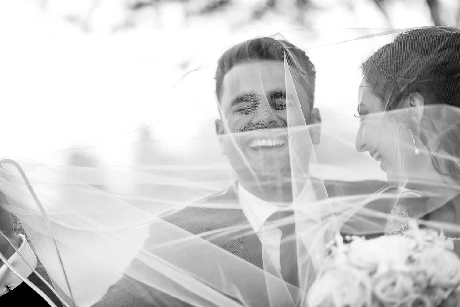 Romantic wedding photo with veil creating soft dreamy effect in natural light.