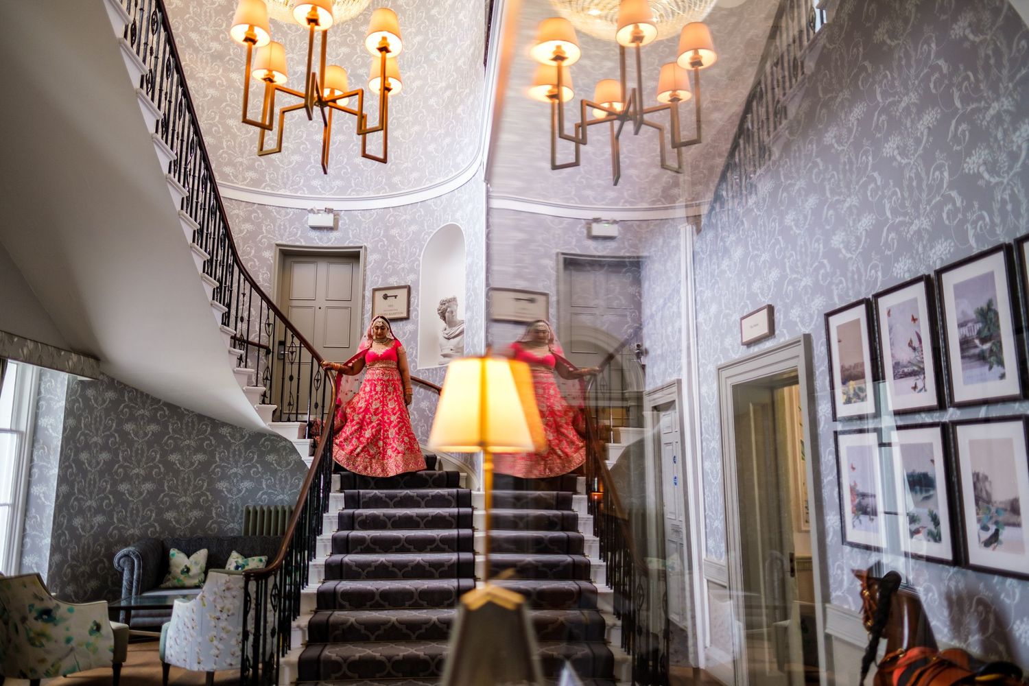 Elegant staircase in historic venue with red dress and vintage chandeliers creating dramatic atmosphere.