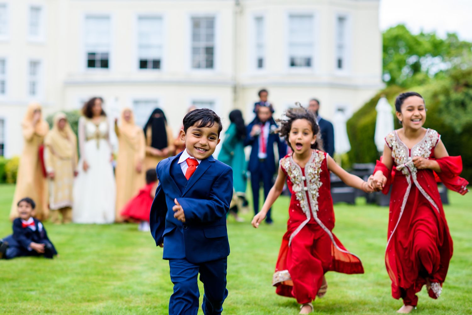 Wedding celebration with guests dancing in formal attire on green lawn.