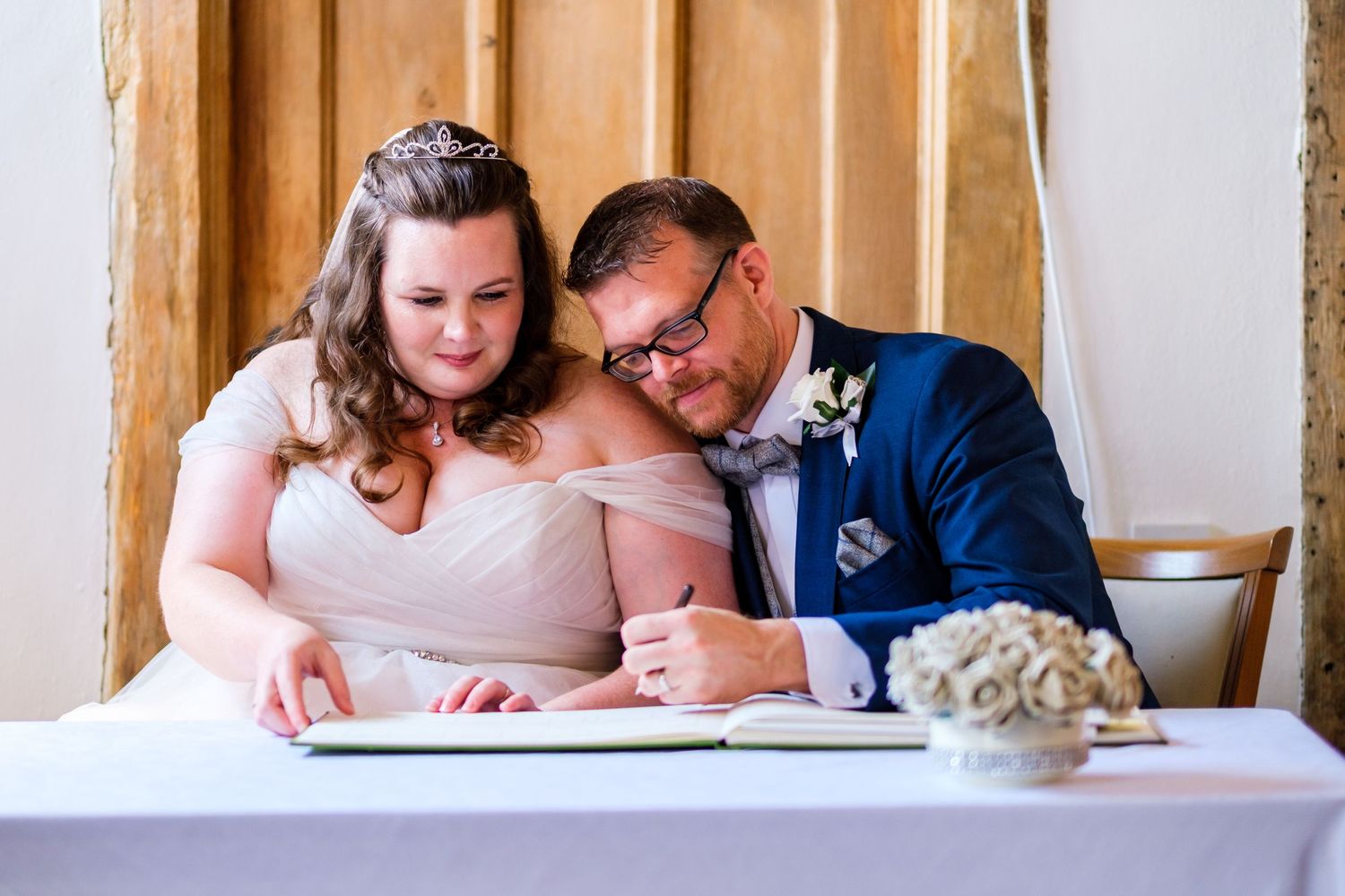 A couple shares an intimate moment while signing papers at a wooden table.