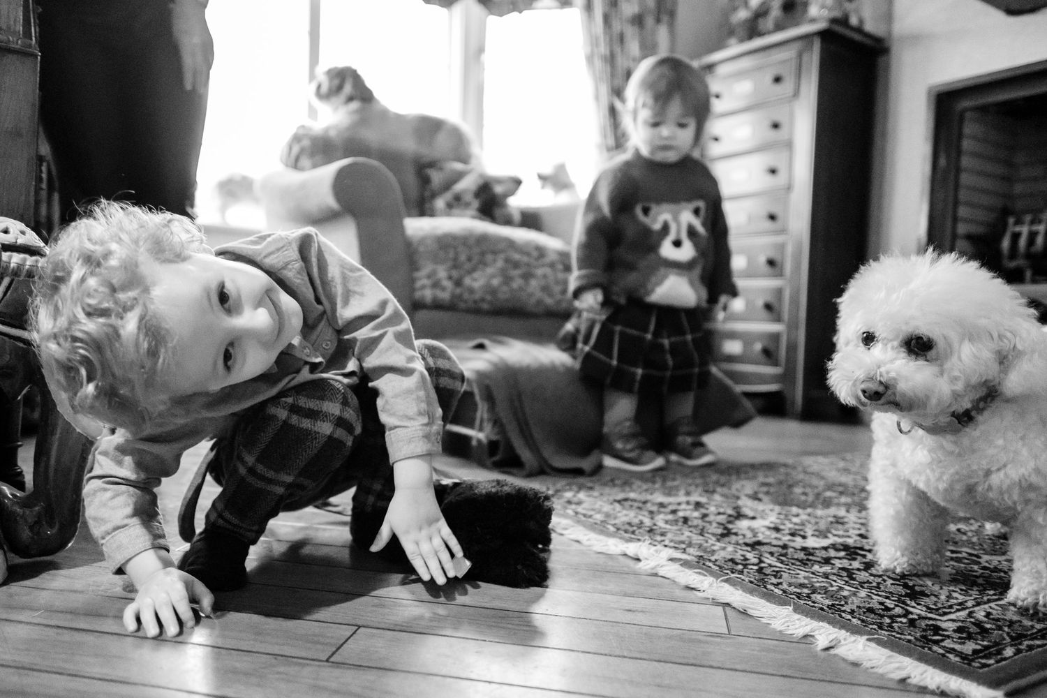 A black and white collage of children playing with and exploring a cat on various floors and surfaces.