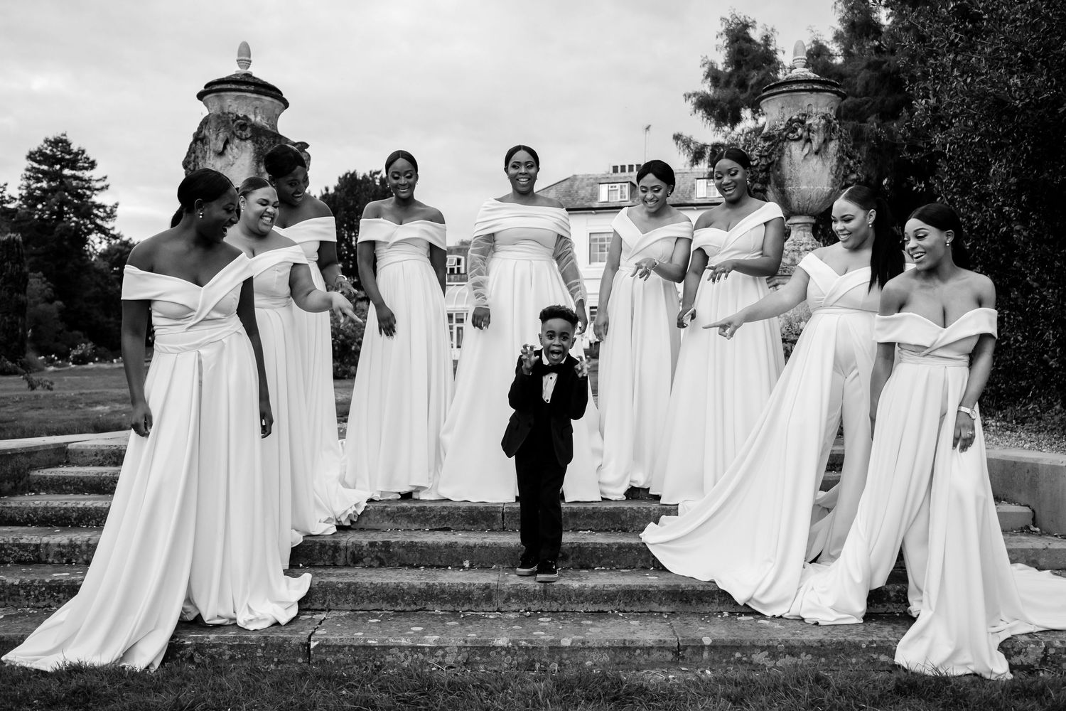 Wedding party members pose in coordinated white dresses on outdoor steps.