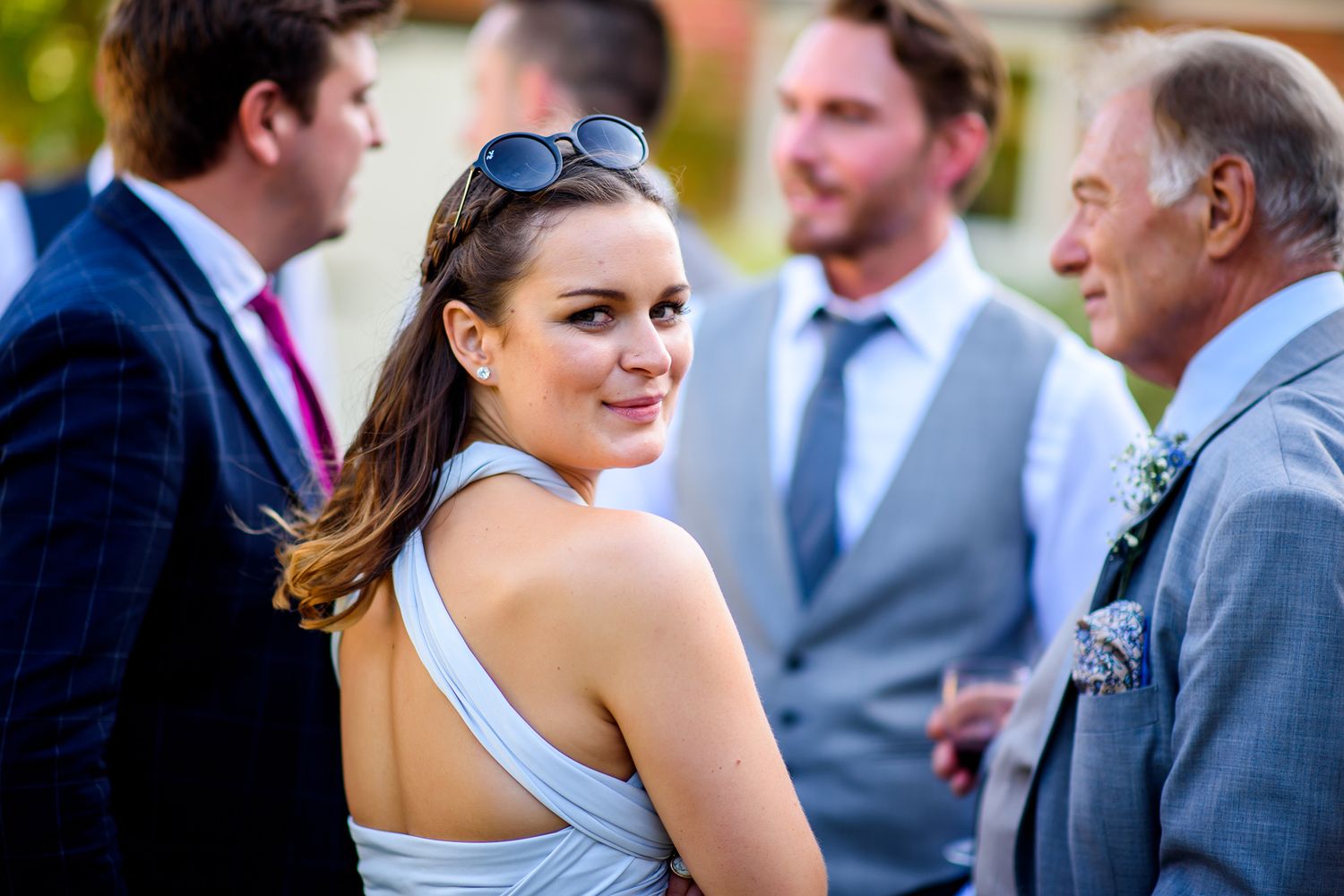 Wedding guests in formal attire mingle during an outdoor summer celebration.