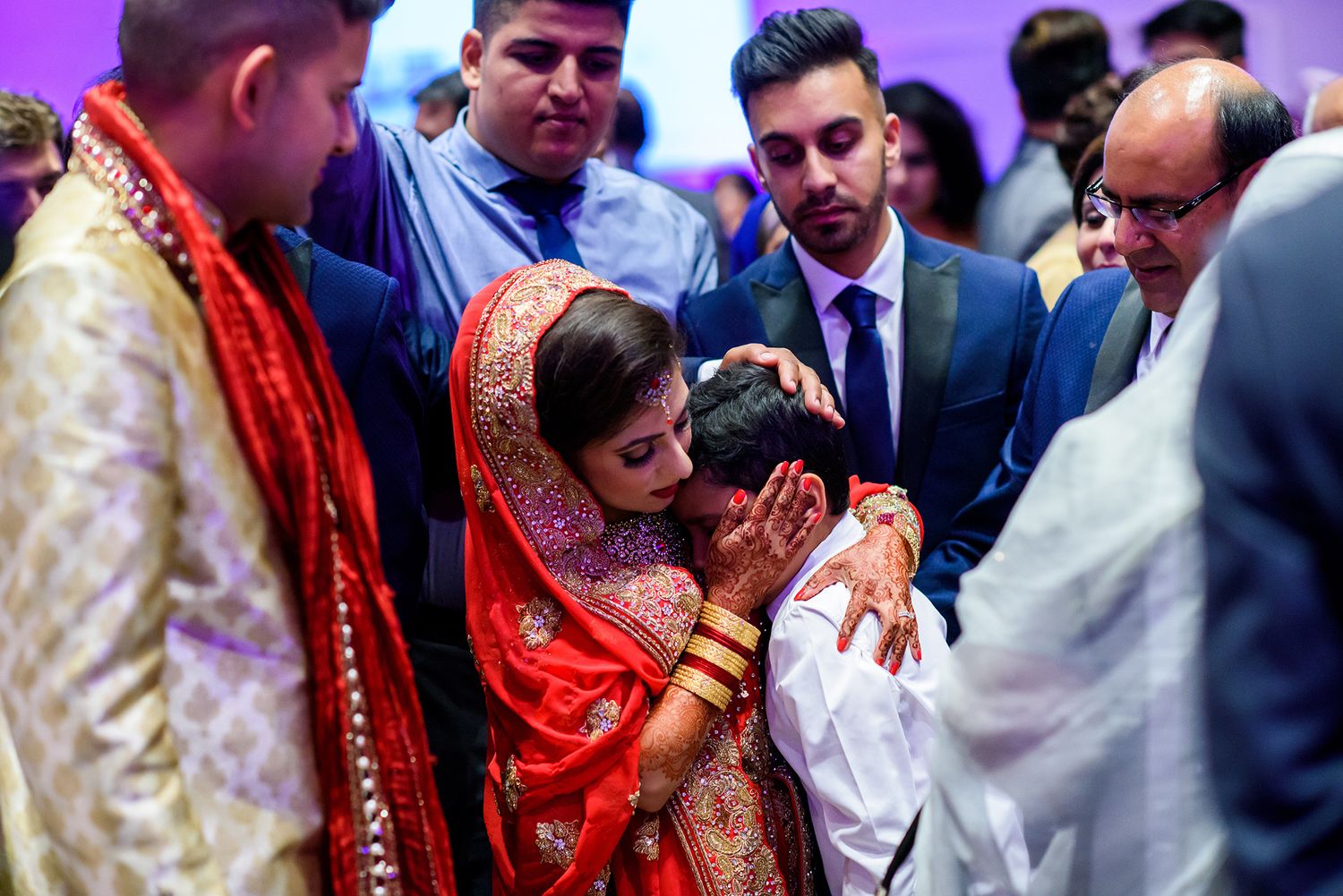 Wedding celebration with guests in traditional attire mingling under purple ambient lighting.