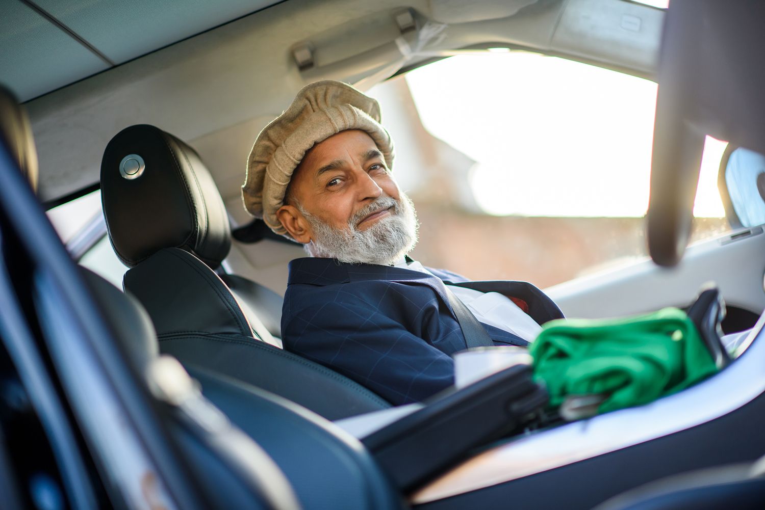 An elderly gentleman with a white beard smiles while sitting in the driver's seat of a car.