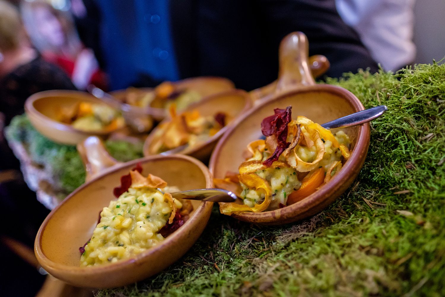 Close-up of decorative appetizers served on wooden bowls with fresh moss garnish at an upscale event.