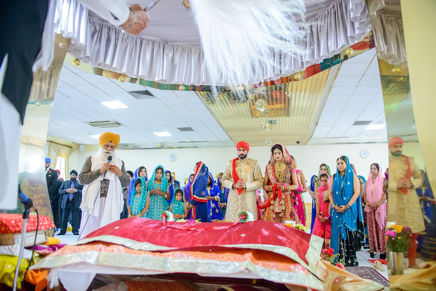 Wedding ceremony setup with white draped ceiling and colorful decorations in an indoor venue.