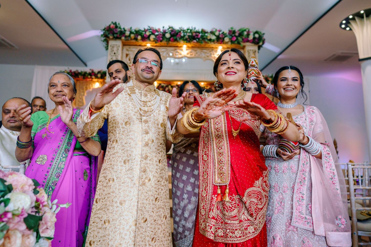 Wedding celebration indoors with decorative floral ceiling arrangements and festive lighting.