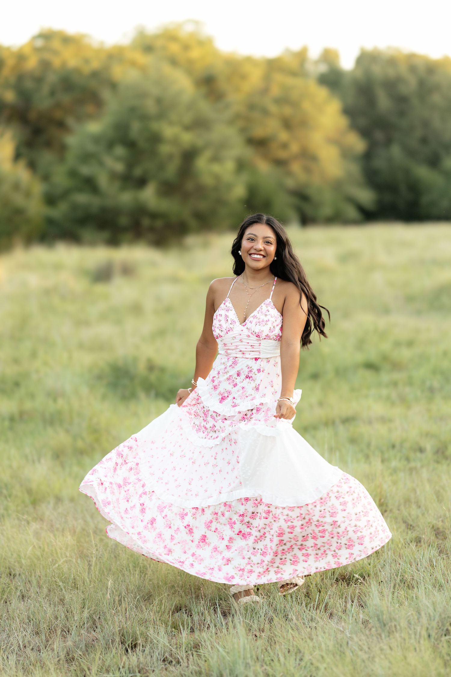 Young woman twirling in a white floral dress in a green meadow, smiling joyfully outdoors.