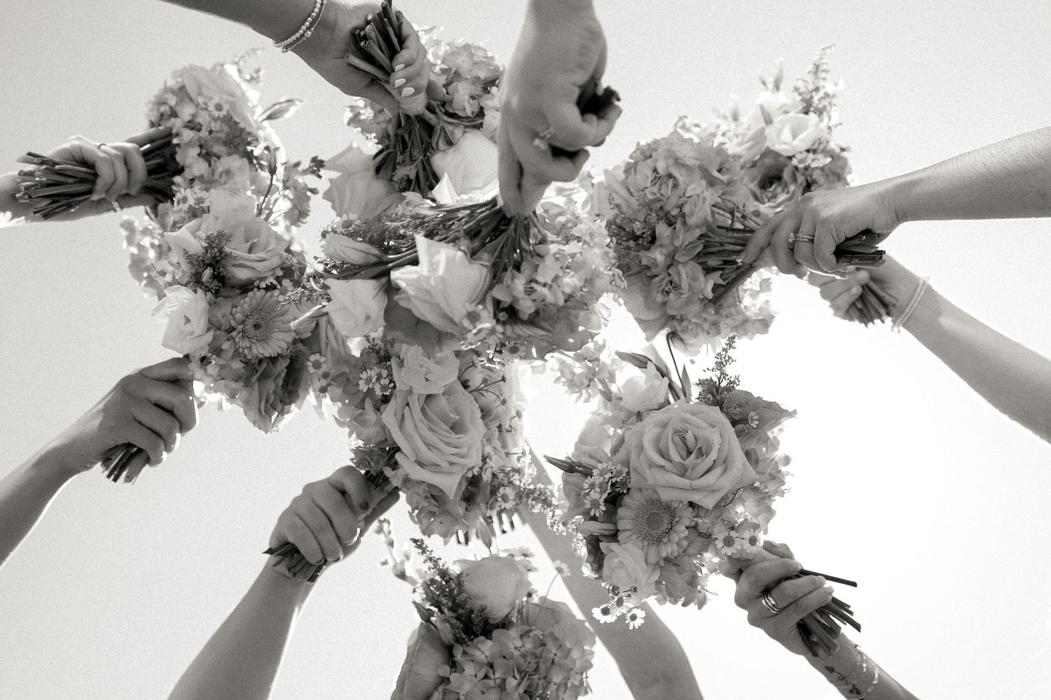 Black and white photo of bridesmaids holding bouquets up together from below.