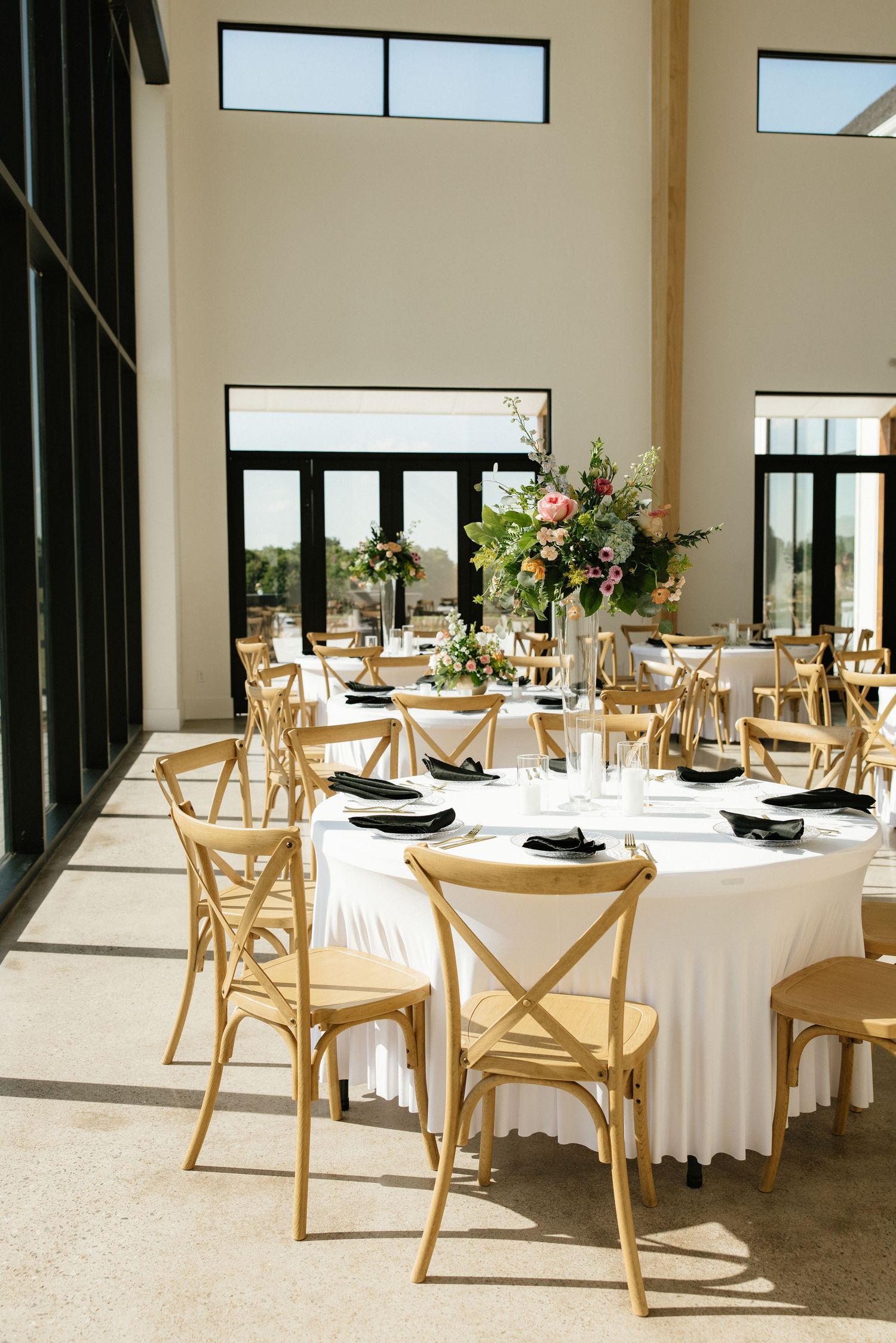 Elegant wedding reception with round tables, white linens, black napkins, and floral centerpieces.