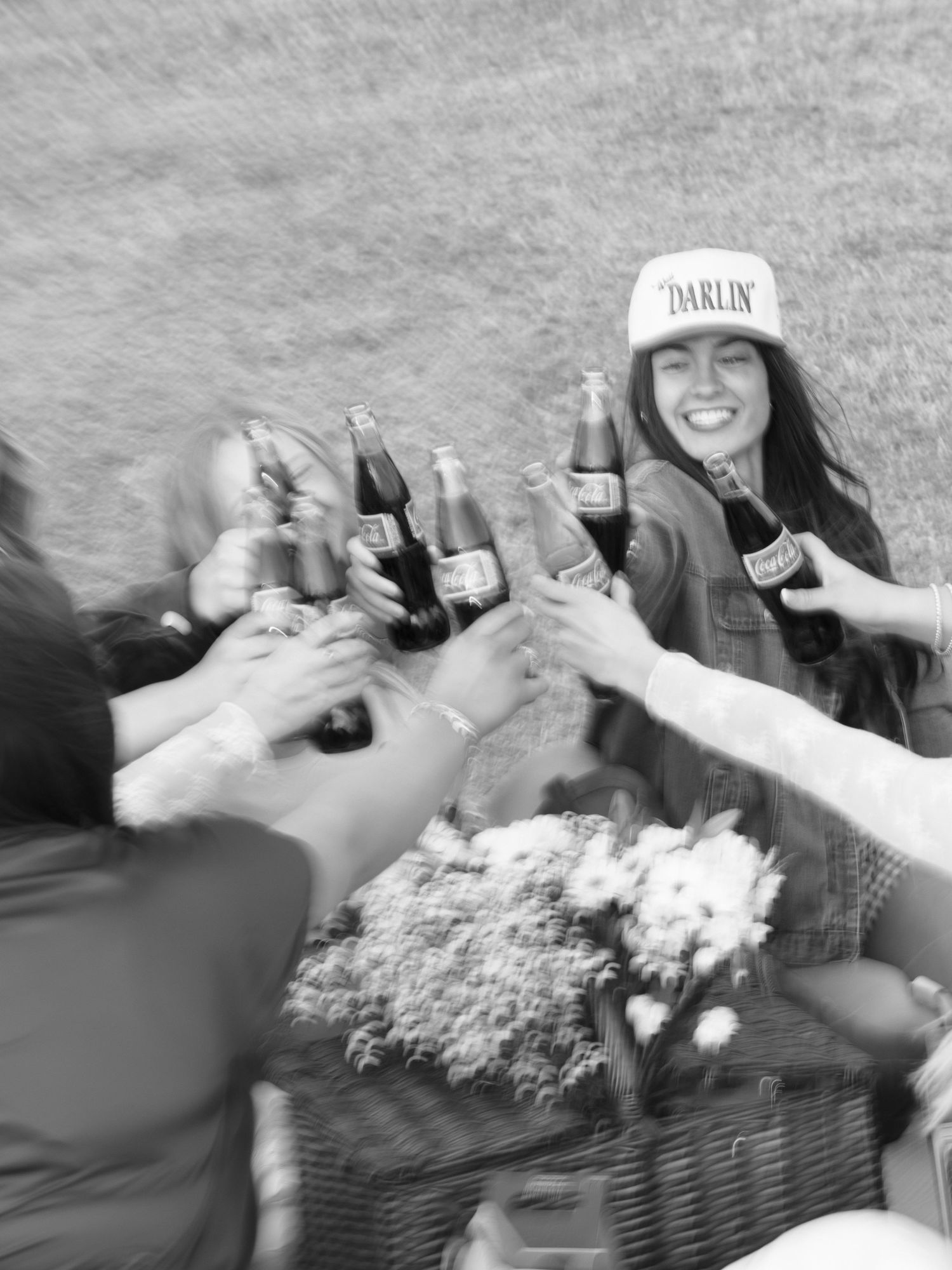 Black and white photo of women toasting Coca-Cola bottles at western bachelorette party picnic.