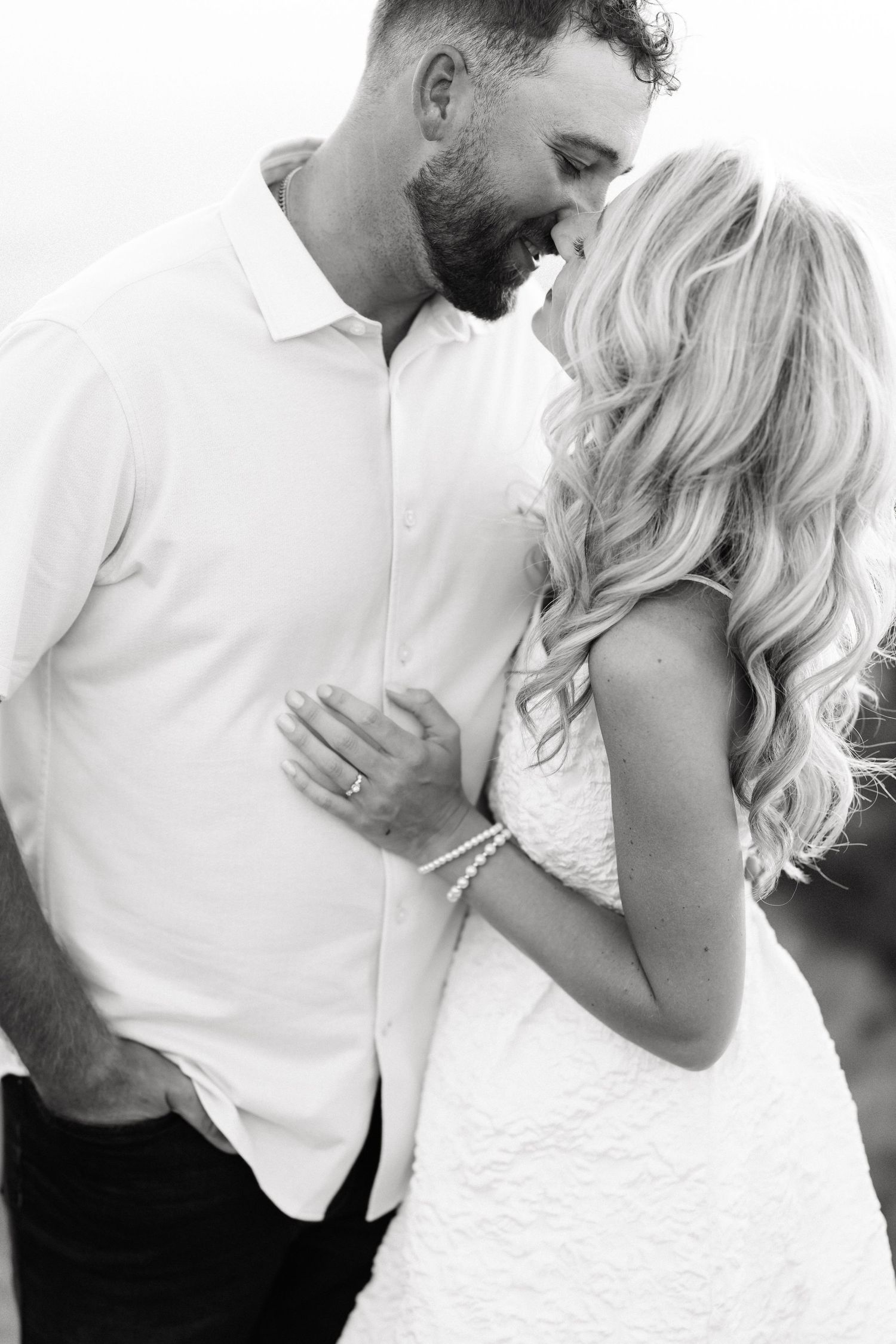 Black and white photo of a smiling couple in wedding attire sharing a romantic moment outdoors.