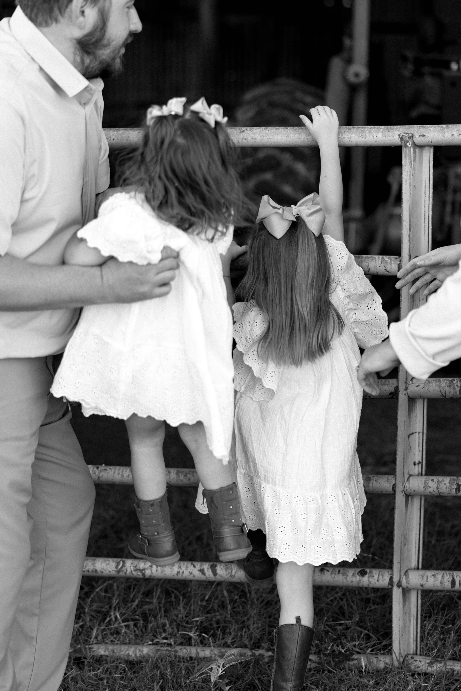 Black and white photo of two young girls in white dresses and boots climbing a wooden fence.
