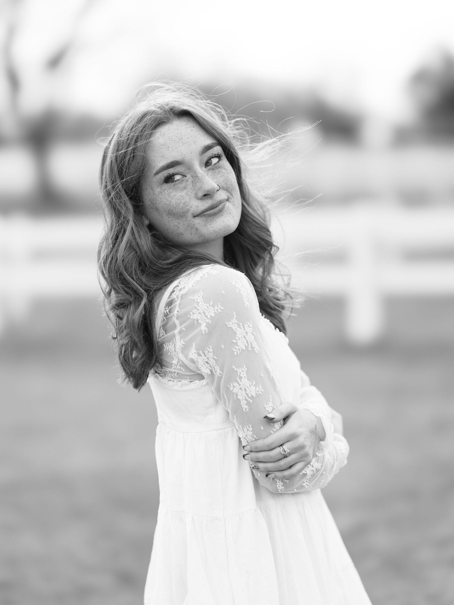 Black and white portrait of smiling girl with freckles in lace dress at horse ranch.