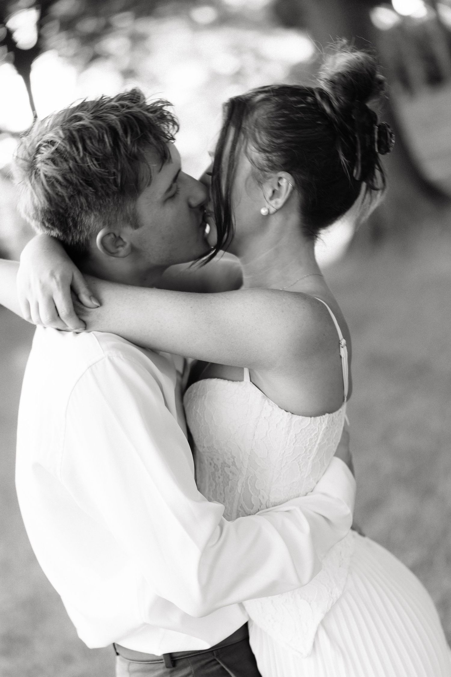 Black and white photo of a couple sharing a romantic kiss outdoors, bride in white dress embracing groom.