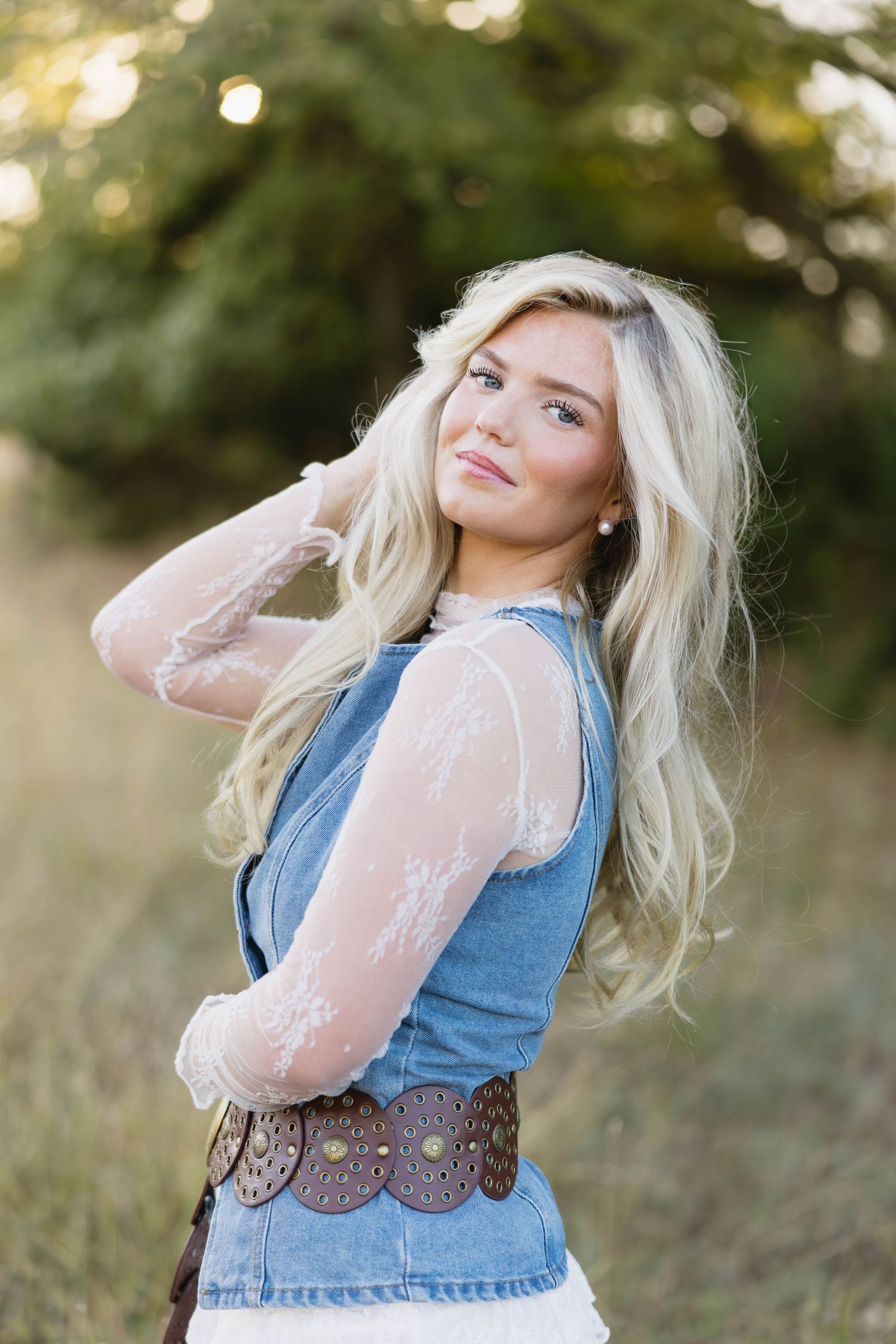 Portrait of a blonde woman in a denim vest and lace sleeves posing in a golden field.
