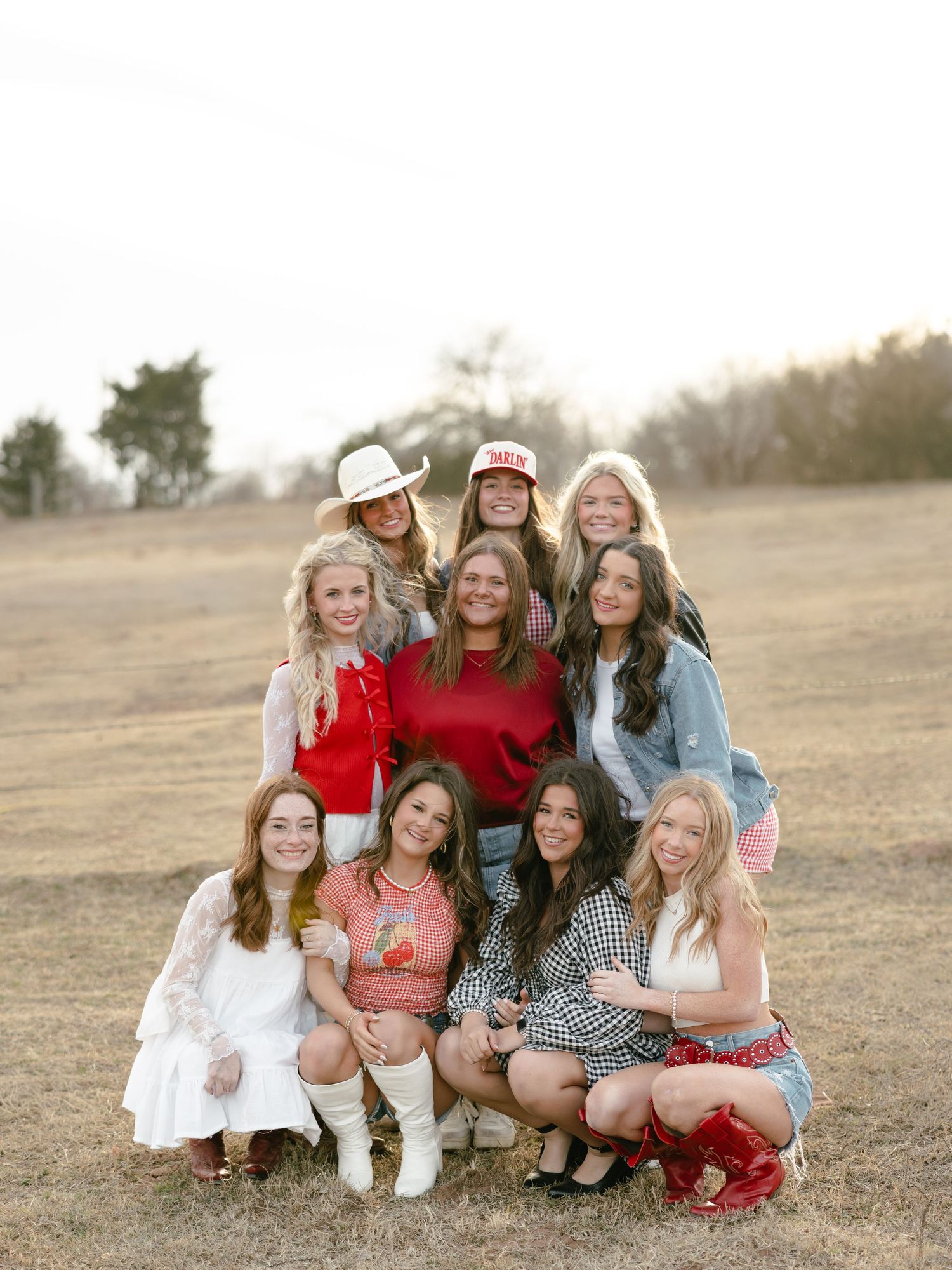 Bachelorette party group posing in two rows in open field wearing western and boho-inspired outfits.