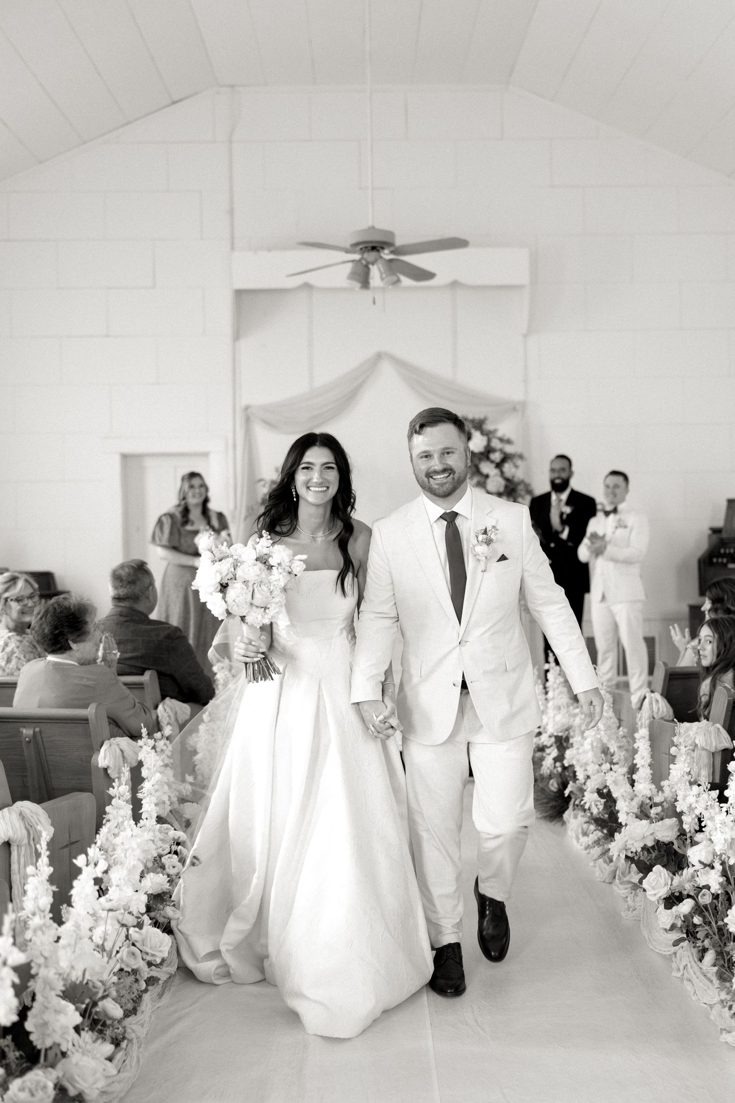 Bride and groom walking down aisle smiling after wedding ceremony in black and white.