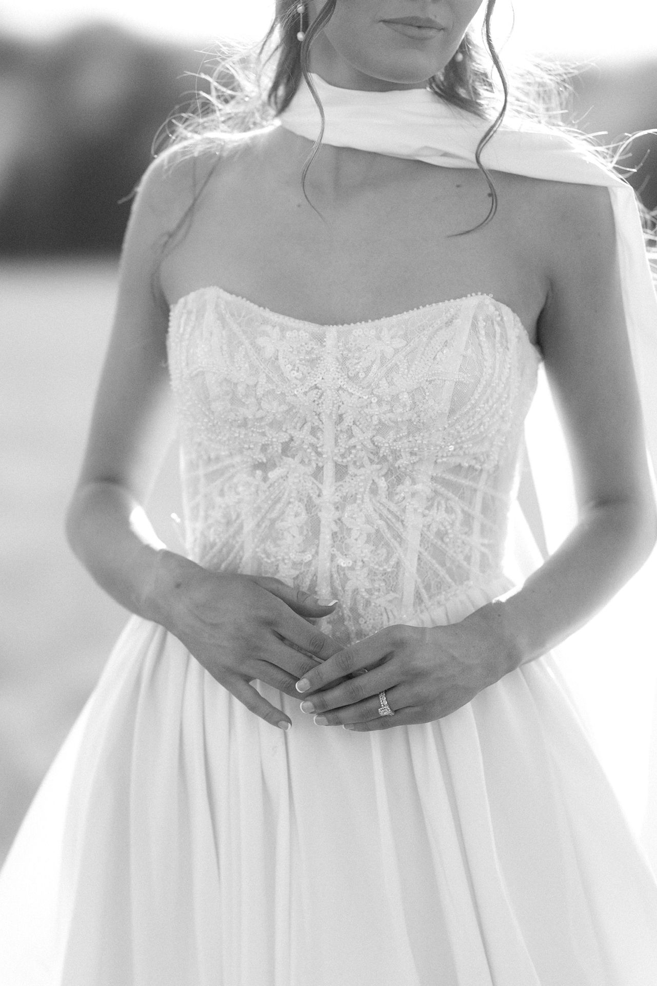 Black and white photo of a bride in a strapless lace corset wedding gown with a choker veil, hands clasped.