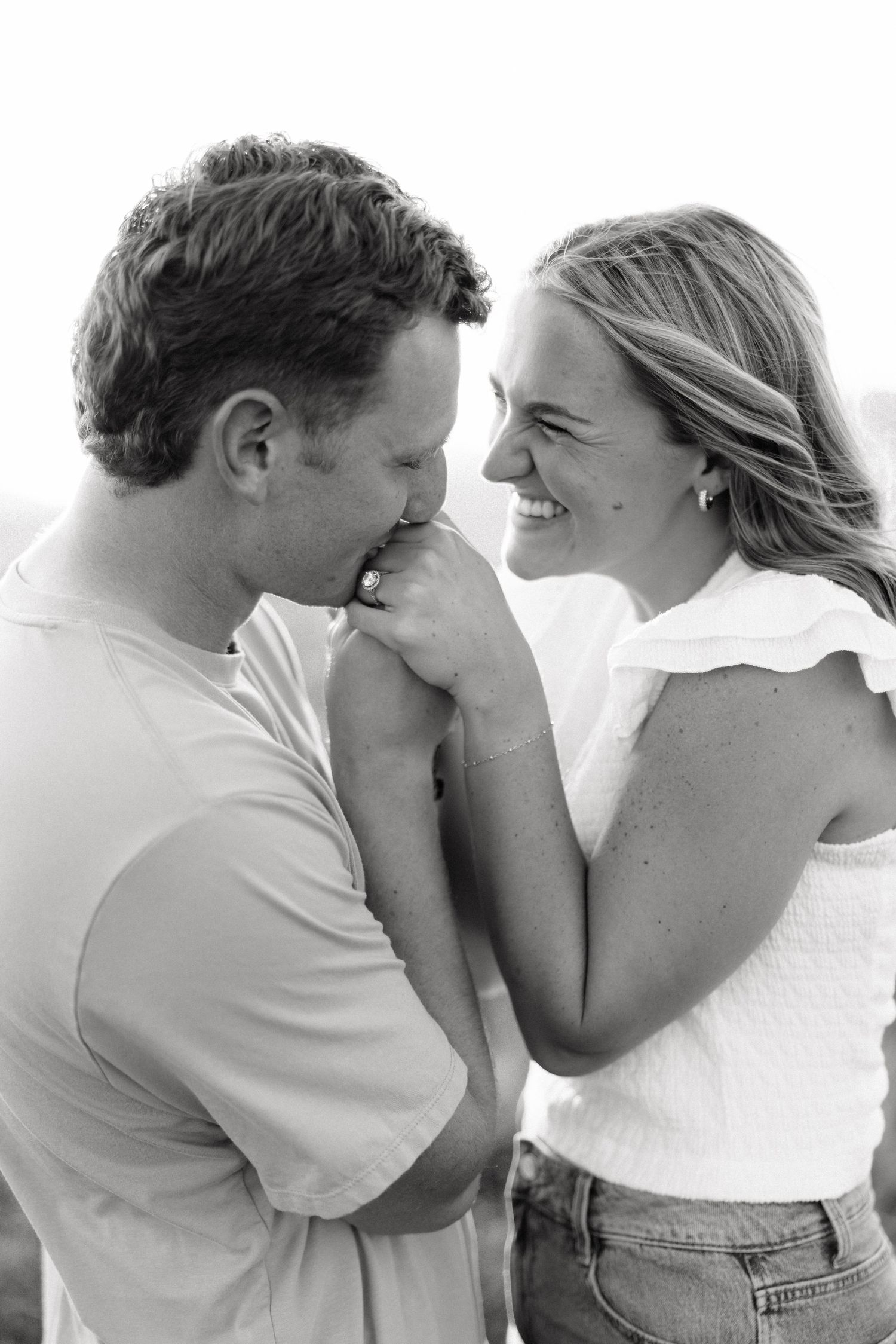 Black and white photo of a smiling couple sharing a tender moment, man kissing woman's hand outdoors.