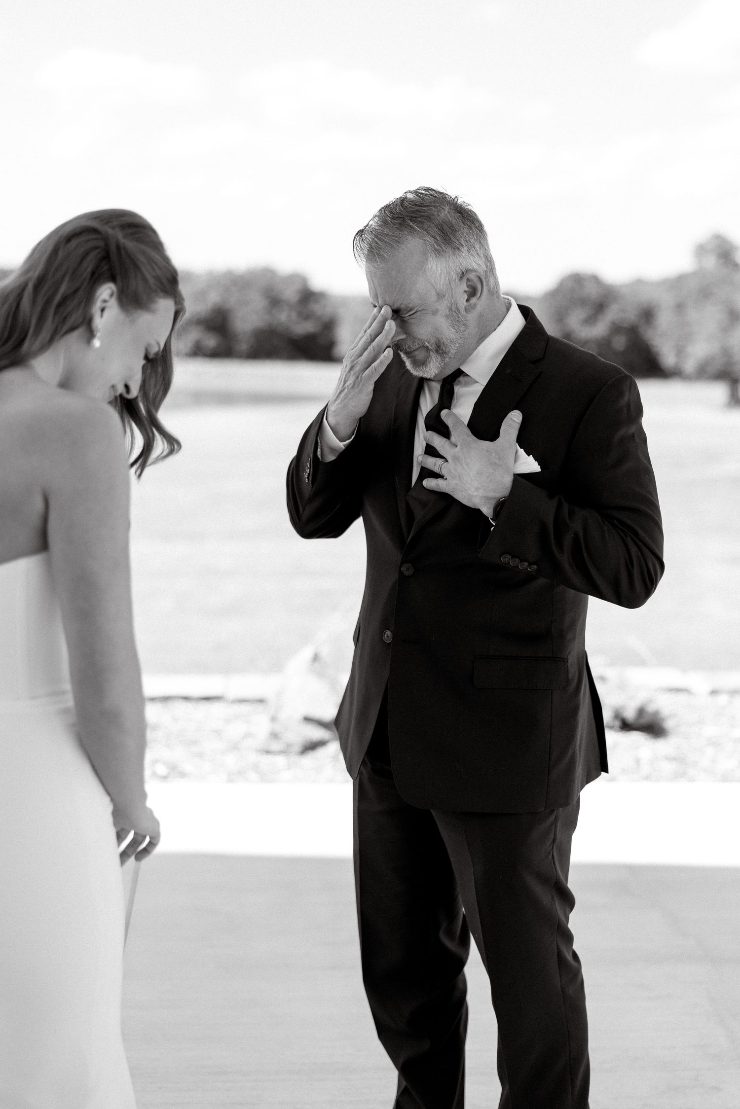 Emotional father wiping tears during first look with bride in black and white photo.