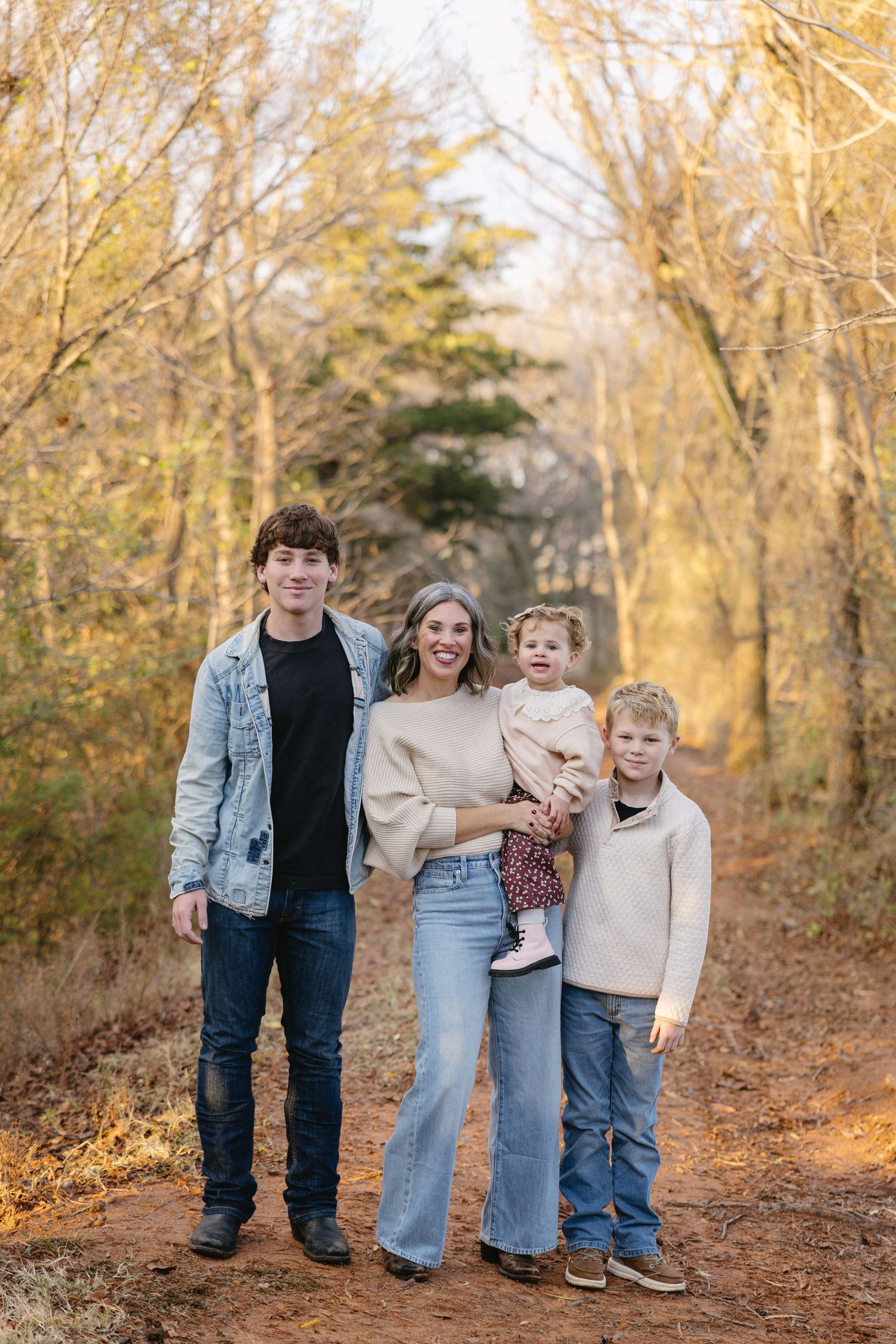 Family of four posing on a dirt path surrounded by golden autumn trees during an outdoor fall photo session.