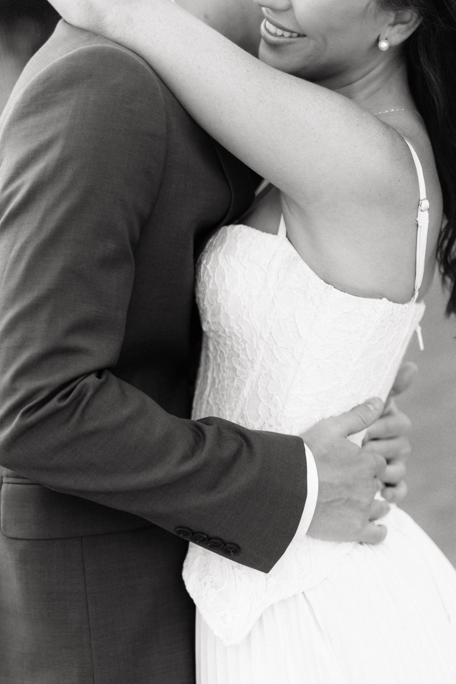 Black and white photo of bride and groom embracing, showcasing wedding dress and suit details.