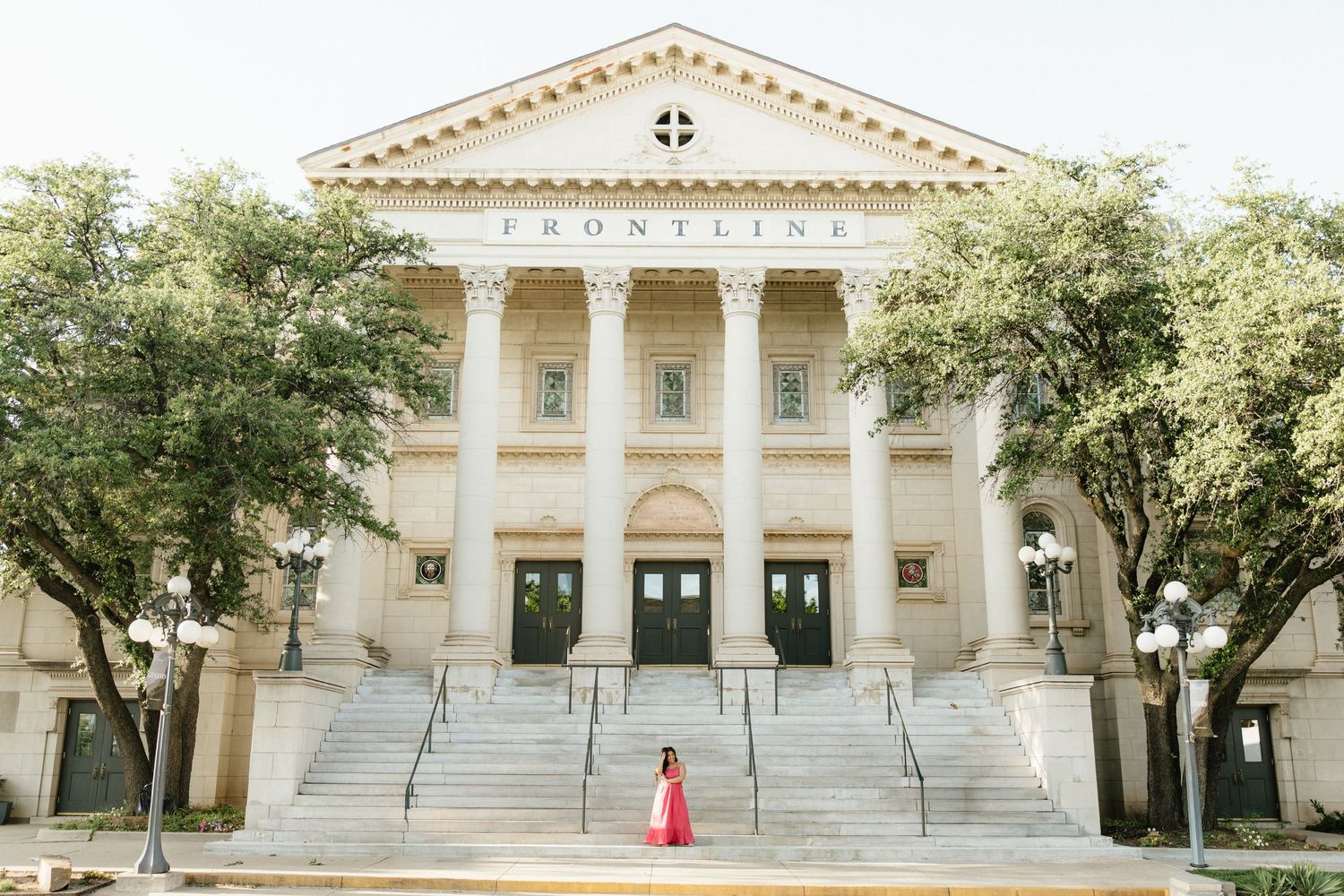 Young woman in red dress standing before the grand Frontline church building with large white columns and steps.