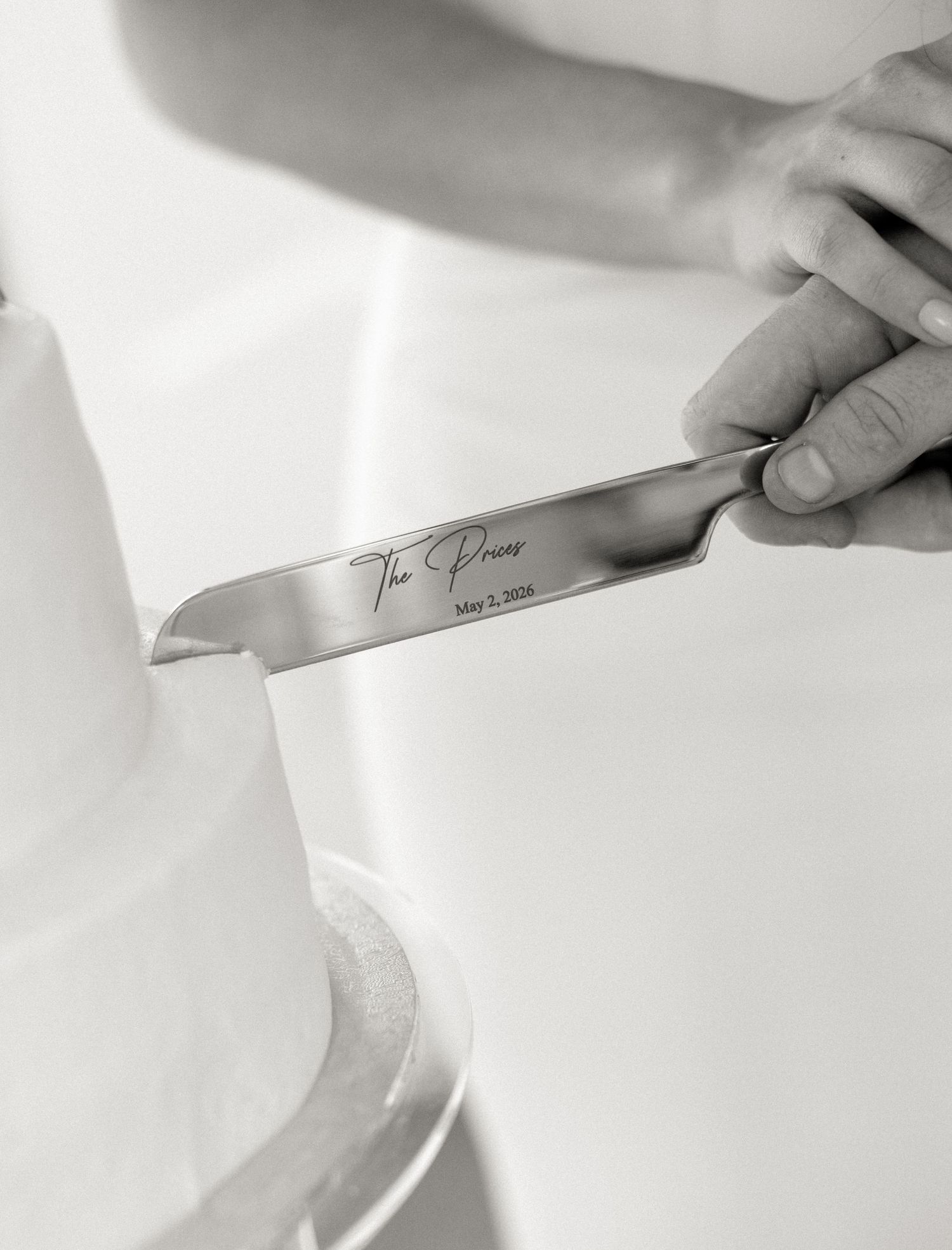 Close-up of personalized engraved cake knife cutting white wedding cake in black and white.