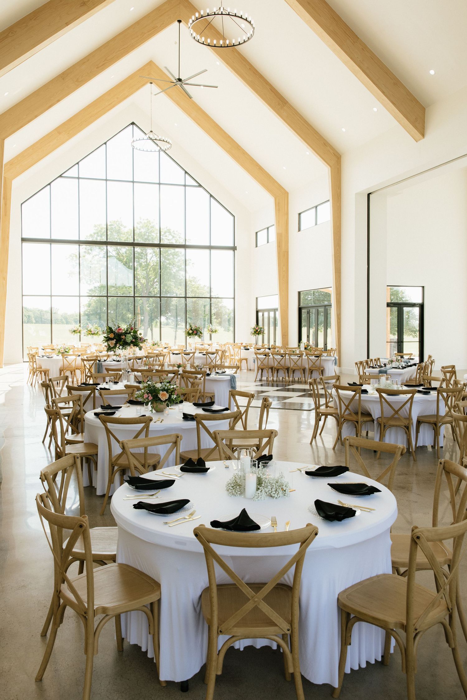 Bright barn wedding venue with vaulted ceilings, wood beams, and round tables set for reception.