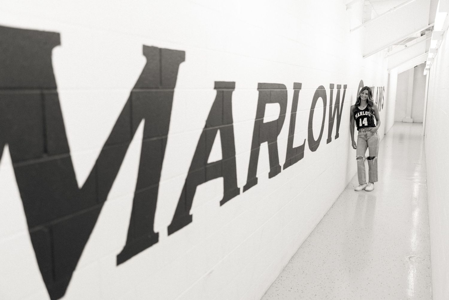 Black and white photo of a person walking past a large Marlow sign on a wall.