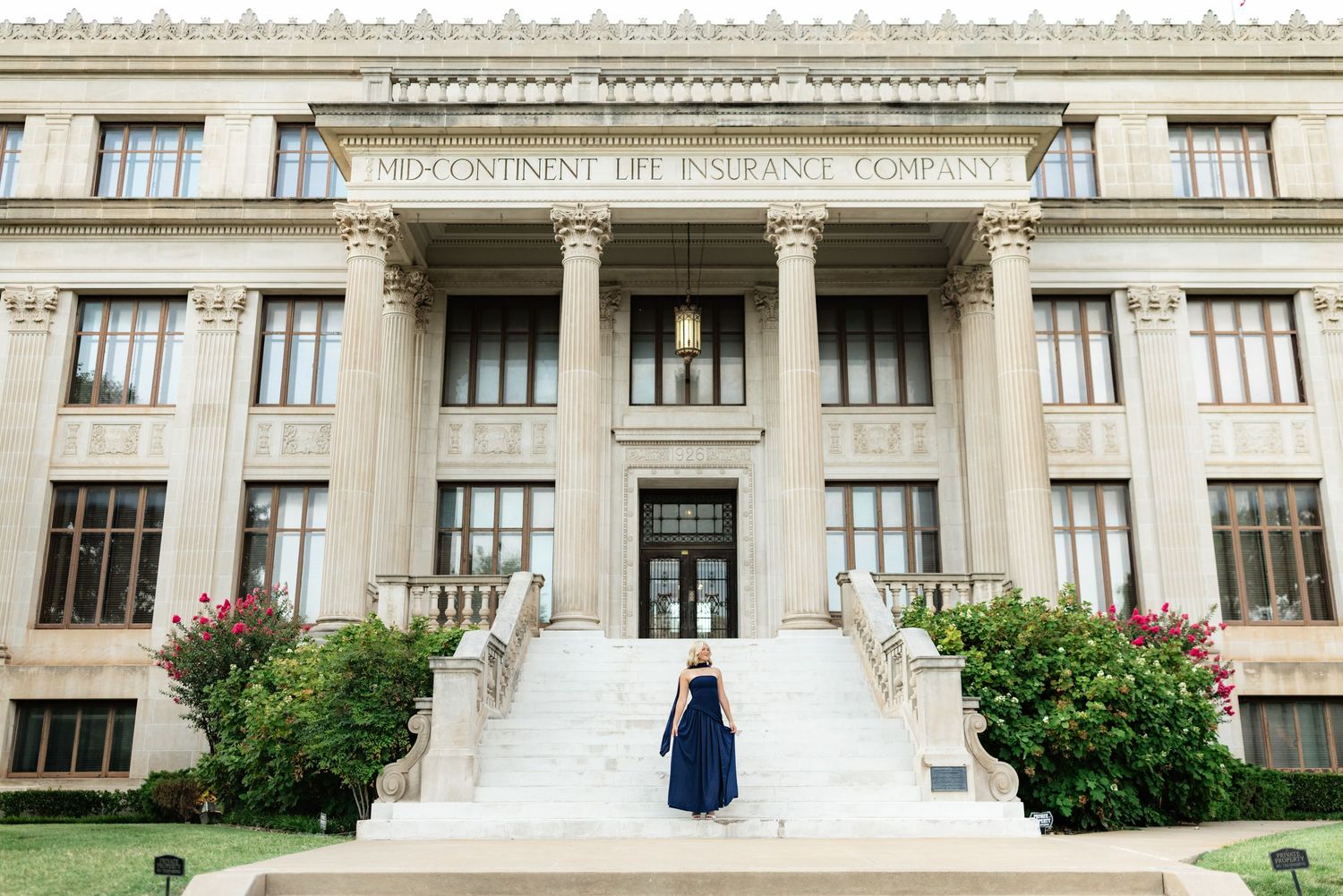 Woman in navy gown ascending steps of Mid-Continent Life Insurance Company building with grand columns.