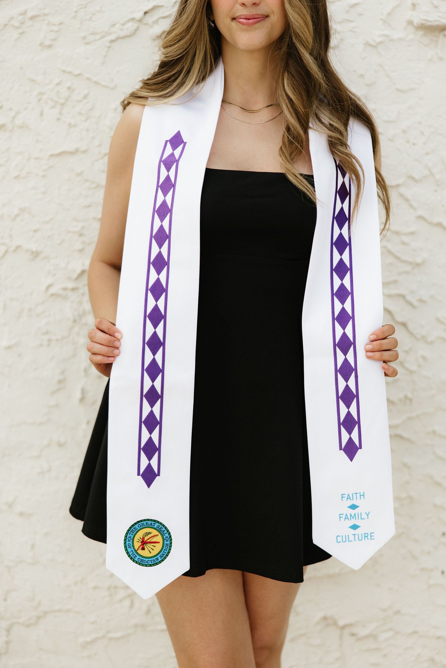Woman in black dress displaying a white and purple graduation stole with Faith Family Culture text.
