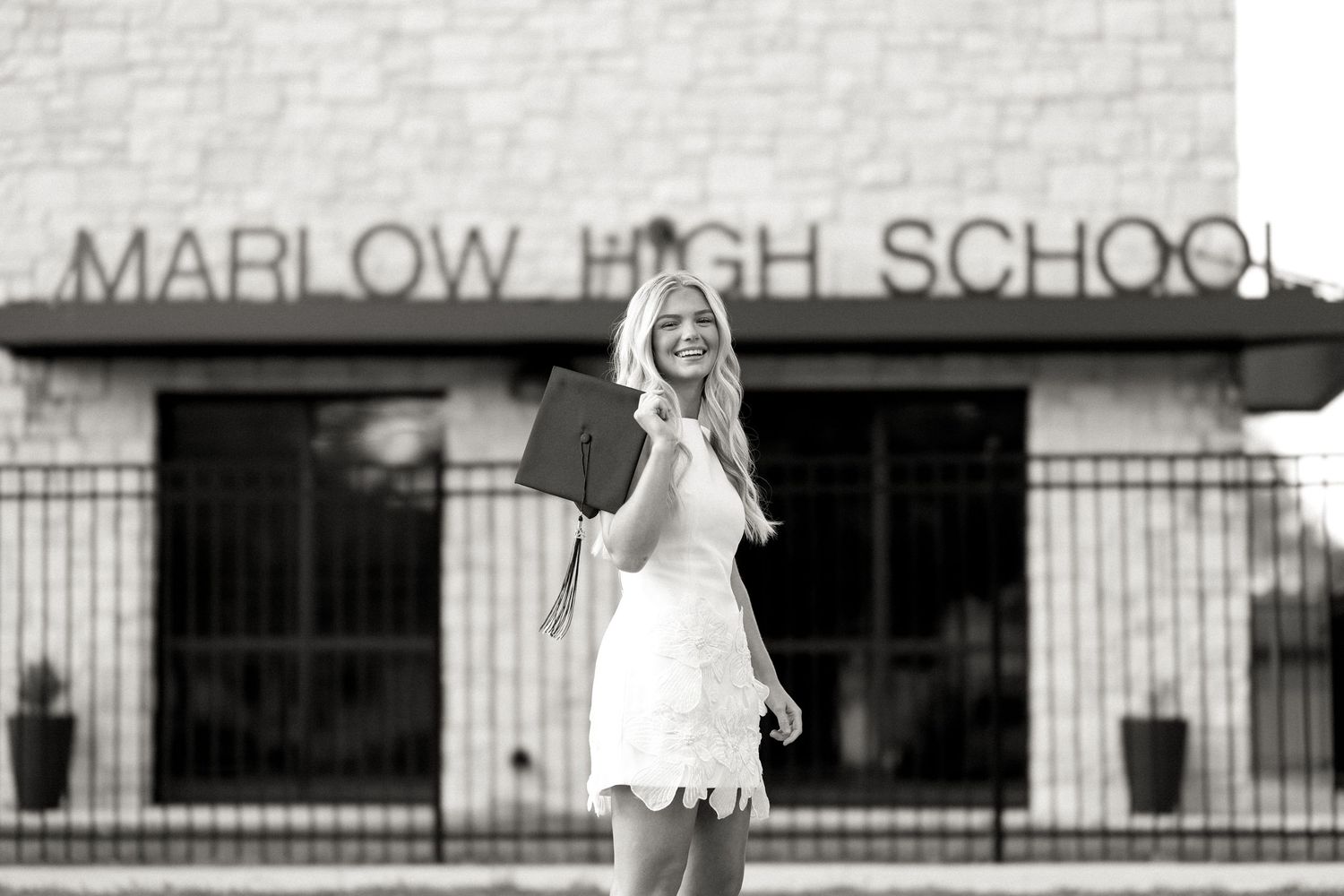 Black and white photo of a smiling woman holding a graduation cap outside Marlow High School.