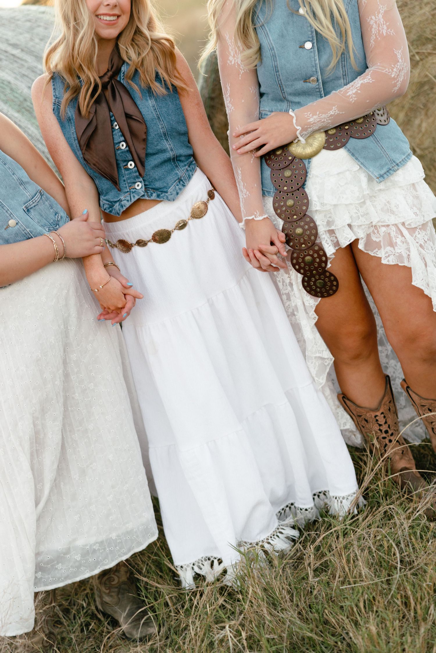Close-up of young women in boho western outfits featuring white skirts, denim vests, and coin belts.