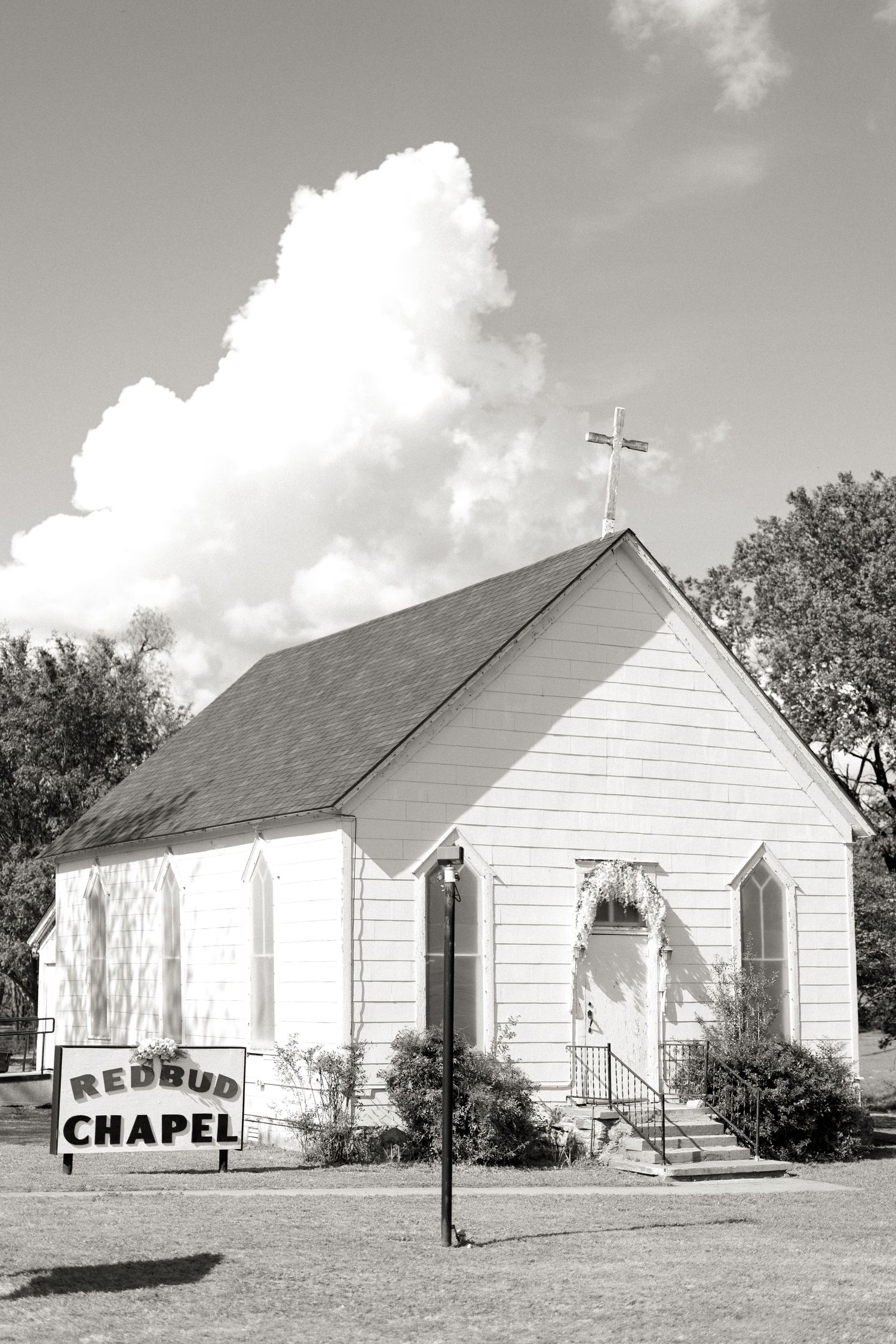 Black and white photo of Redbud Chapel, a small white country church with cross and sign out front.