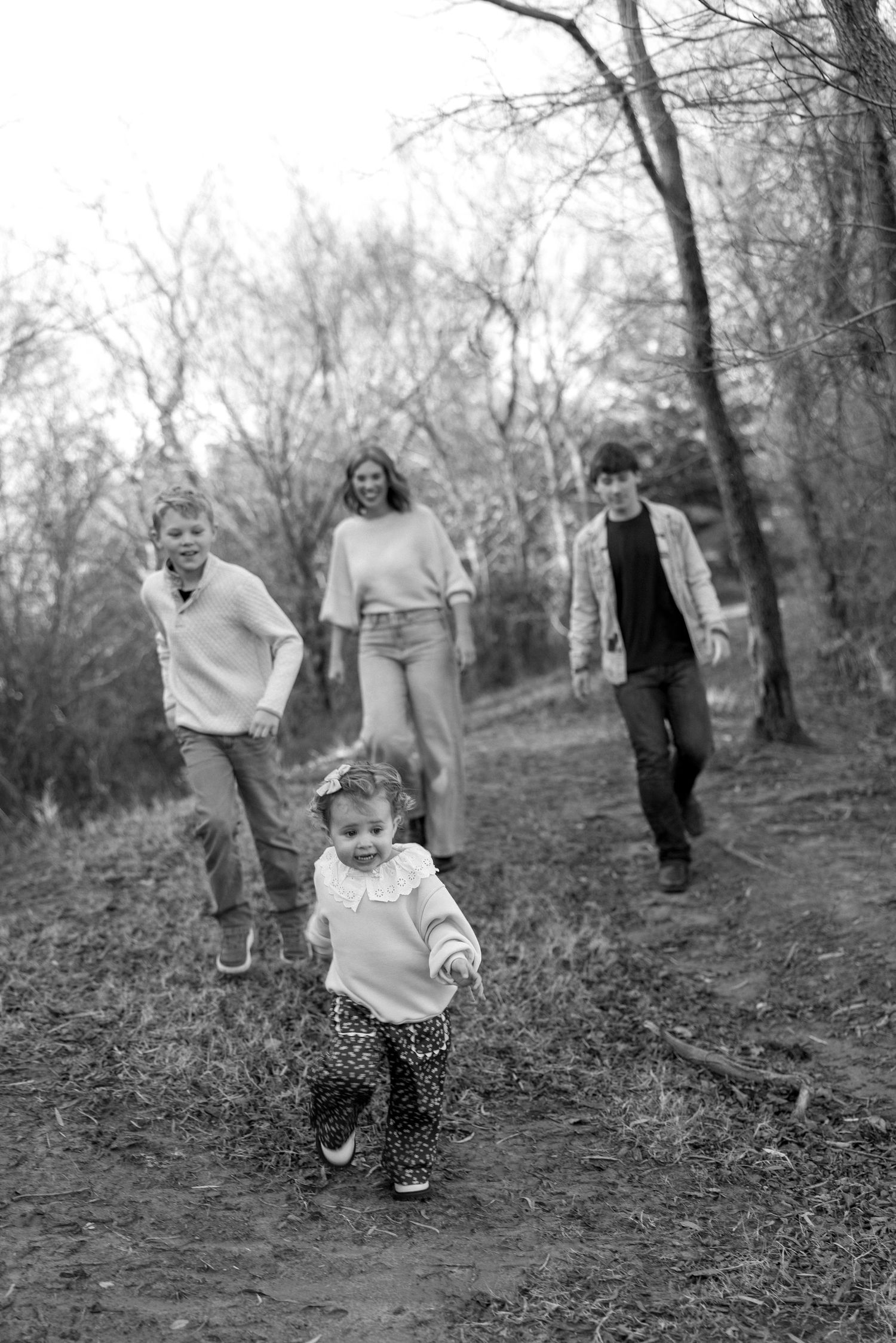 Black and white photo of a family with three kids running and playing on a wooded trail in autumn.
