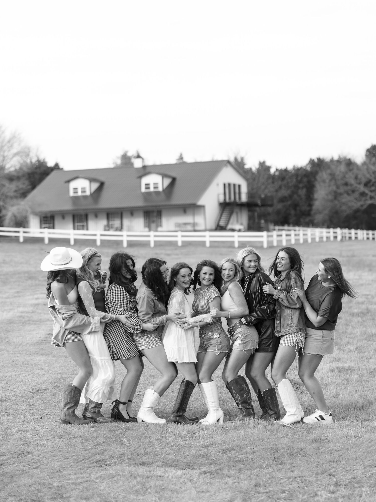 Black and white photo of a large group of young women posing together in a field near a white farmhouse.