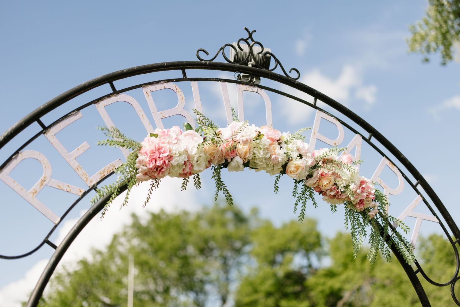 Black iron circular wedding arch decorated with pink and white flowers at Redbud Chapel outdoor ceremony.