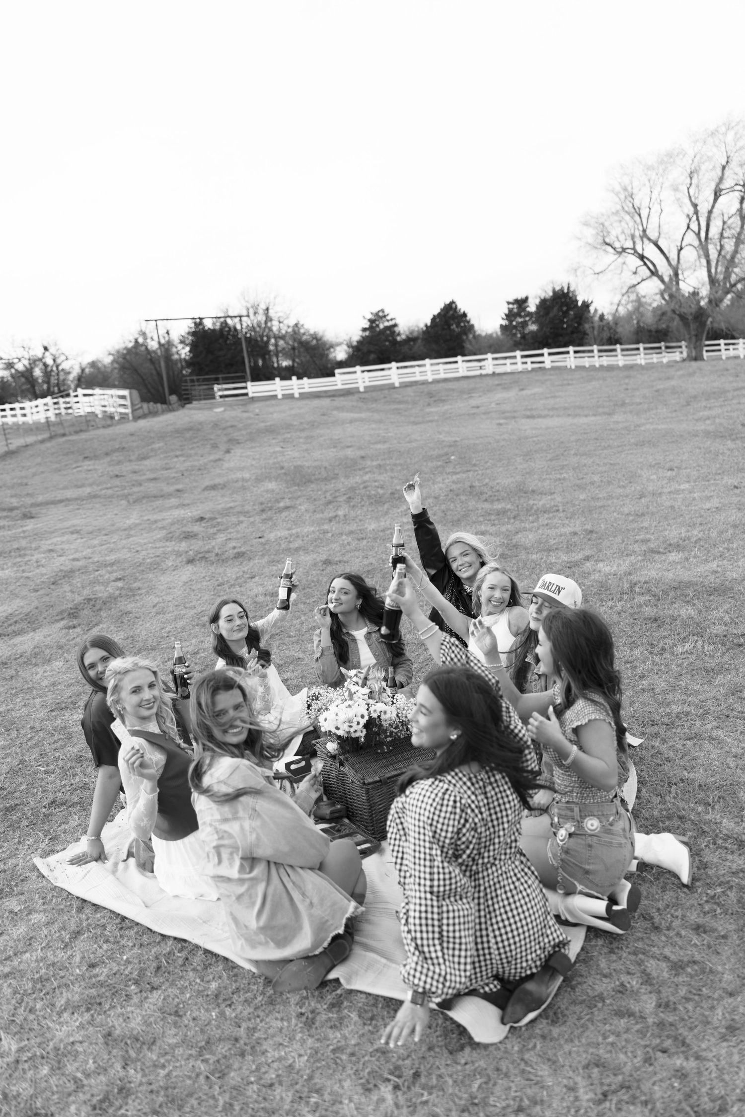Black and white photo of women celebrating at outdoor picnic on farm raising Coca-Cola bottles.