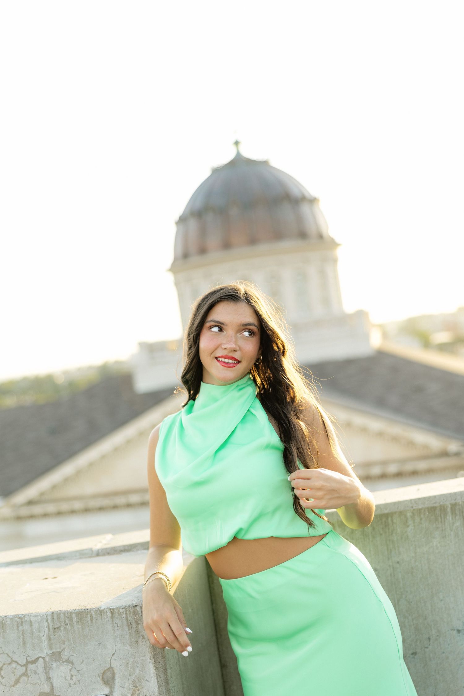 Young woman in mint green two-piece outfit poses outdoors near a domed building in bright sunlight.