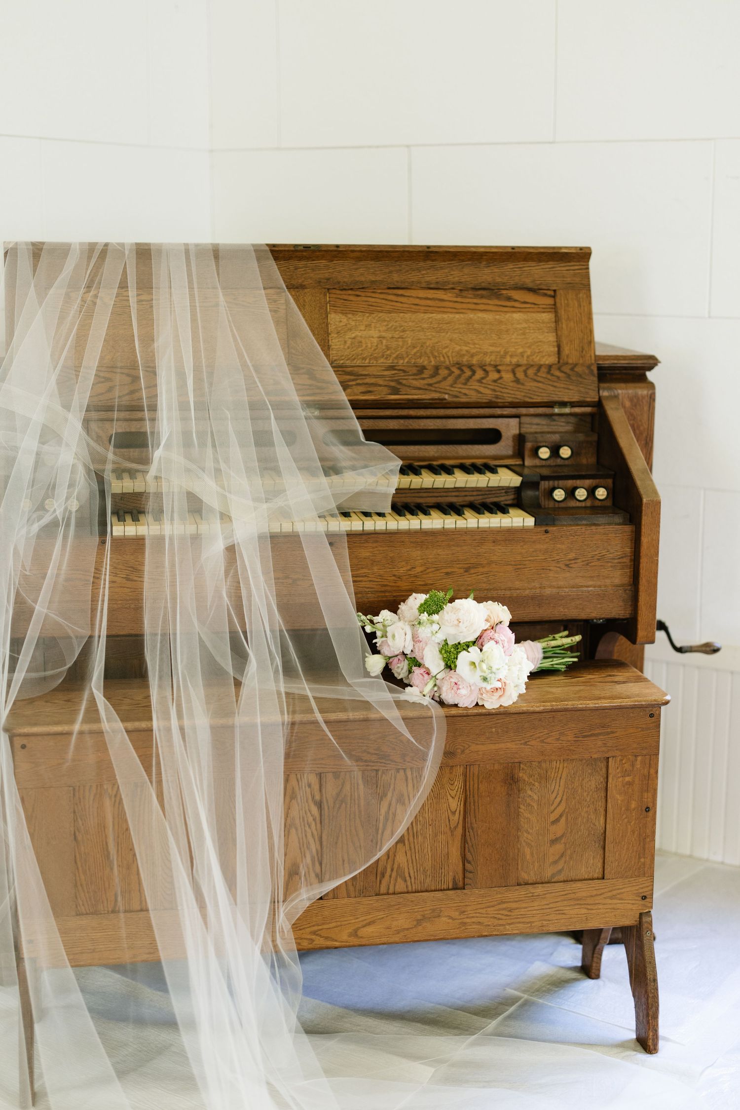 Bridal veil draped over vintage wooden organ with pink bouquet inside white chapel.