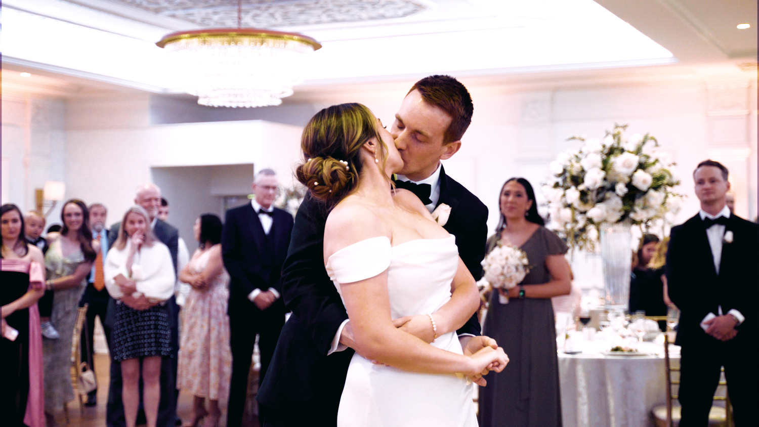 Wedding reception ballroom with couples dancing under soft pink lighting.