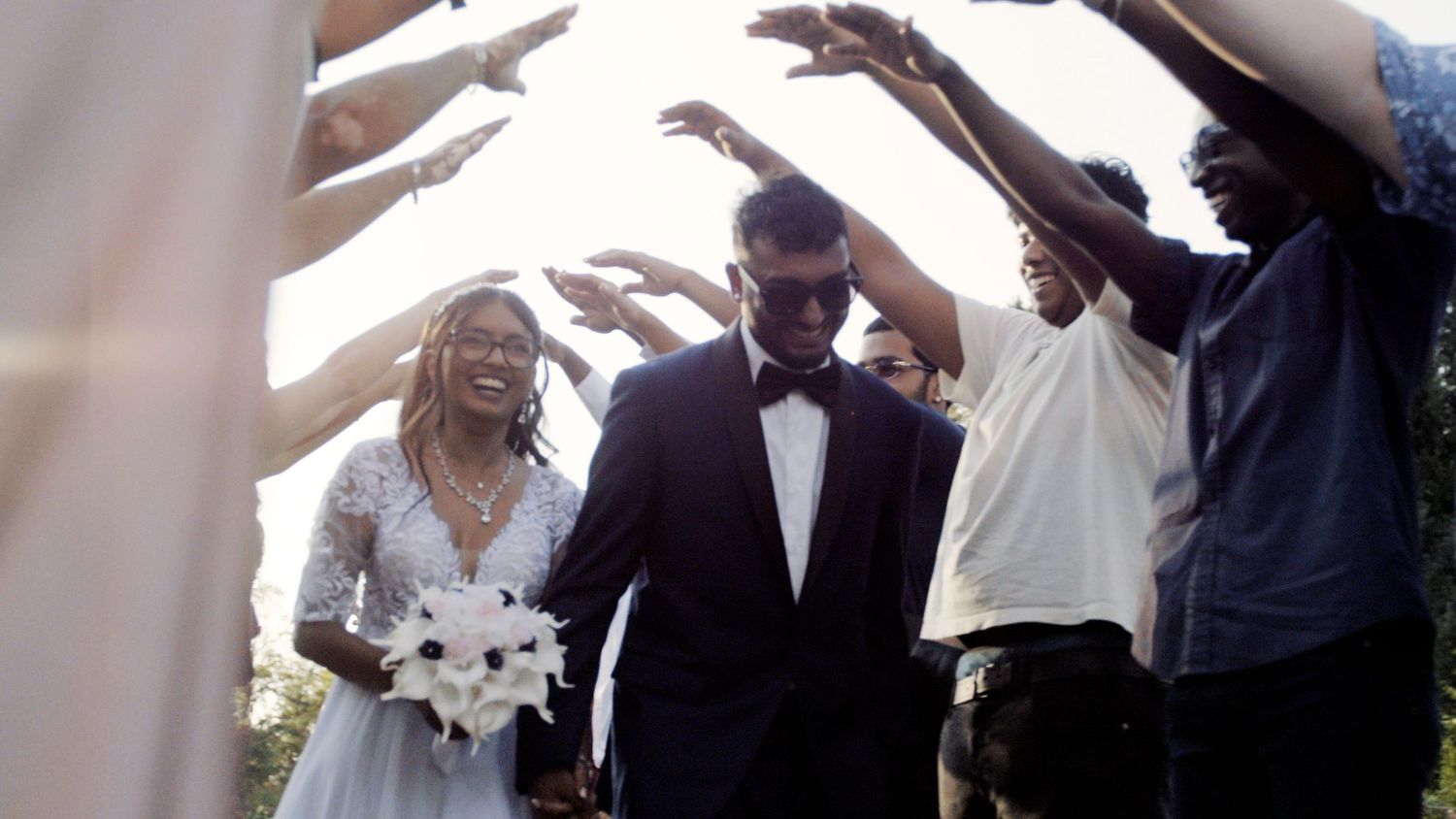Wedding party members raising arms to form a tunnel or archway outdoors.