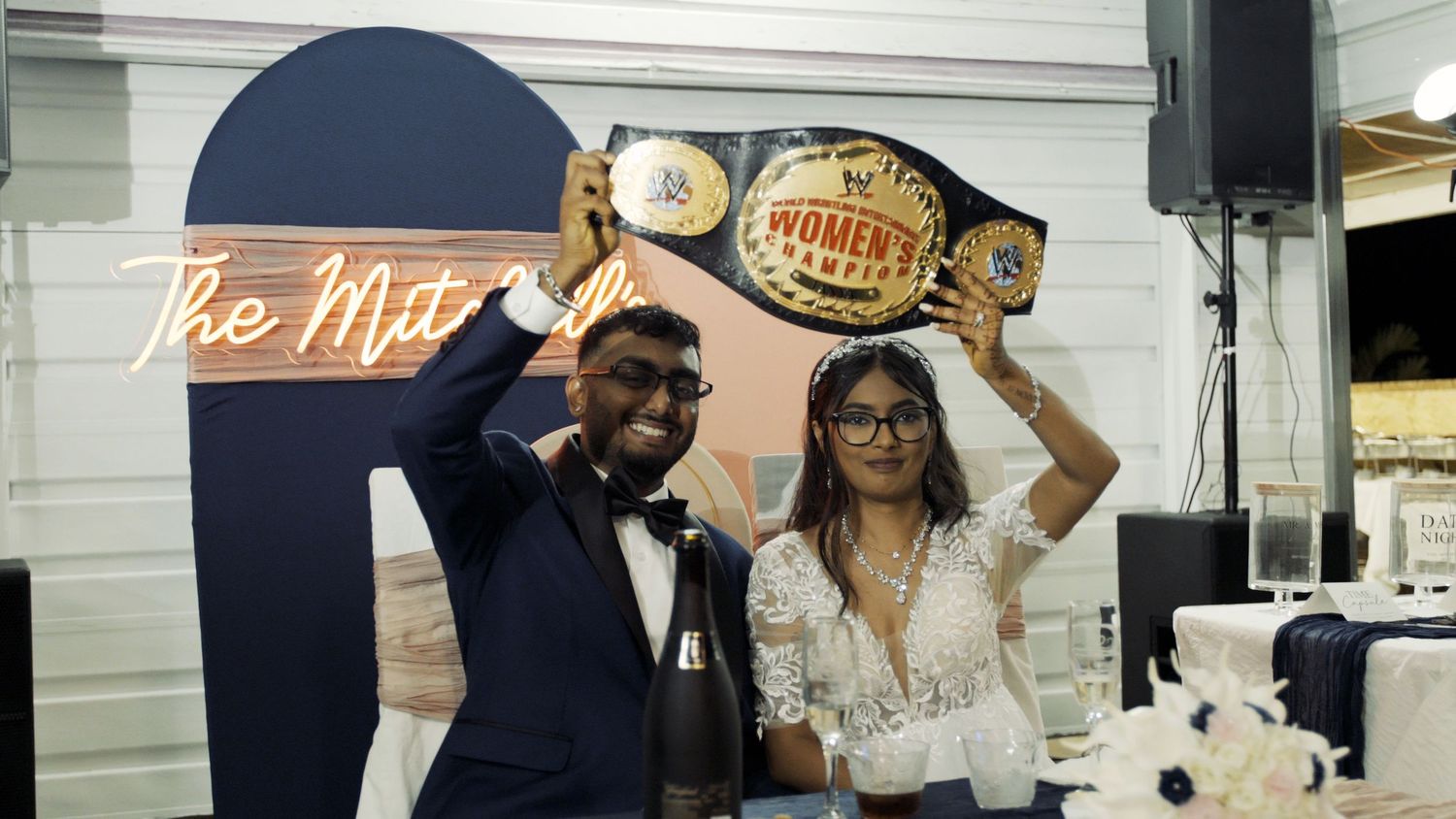 Indoor wedding reception setup with signs and decor against white paneled walls.