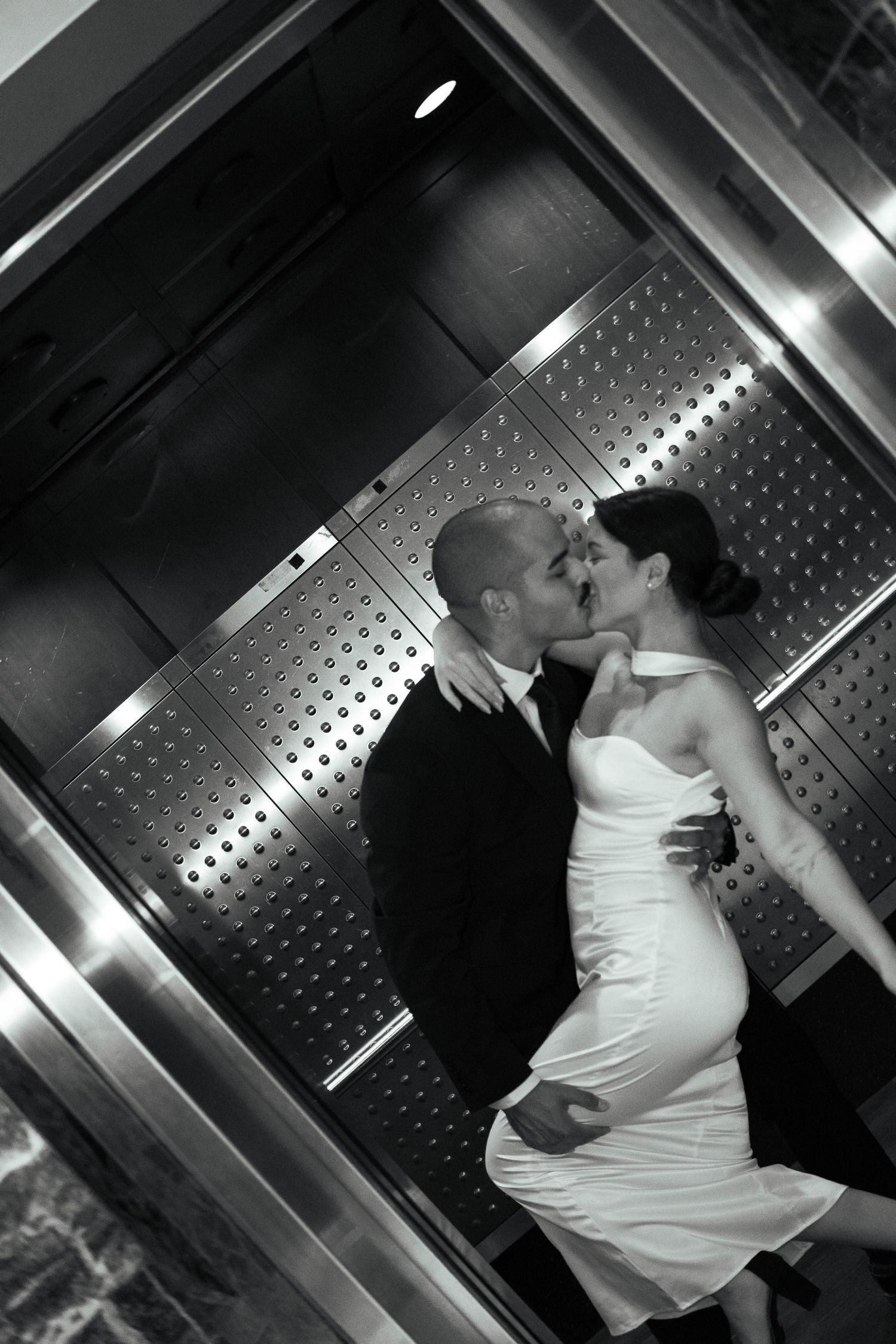 Bride and groom sharing a tender kiss inside an elevator in a black and white wedding photo.