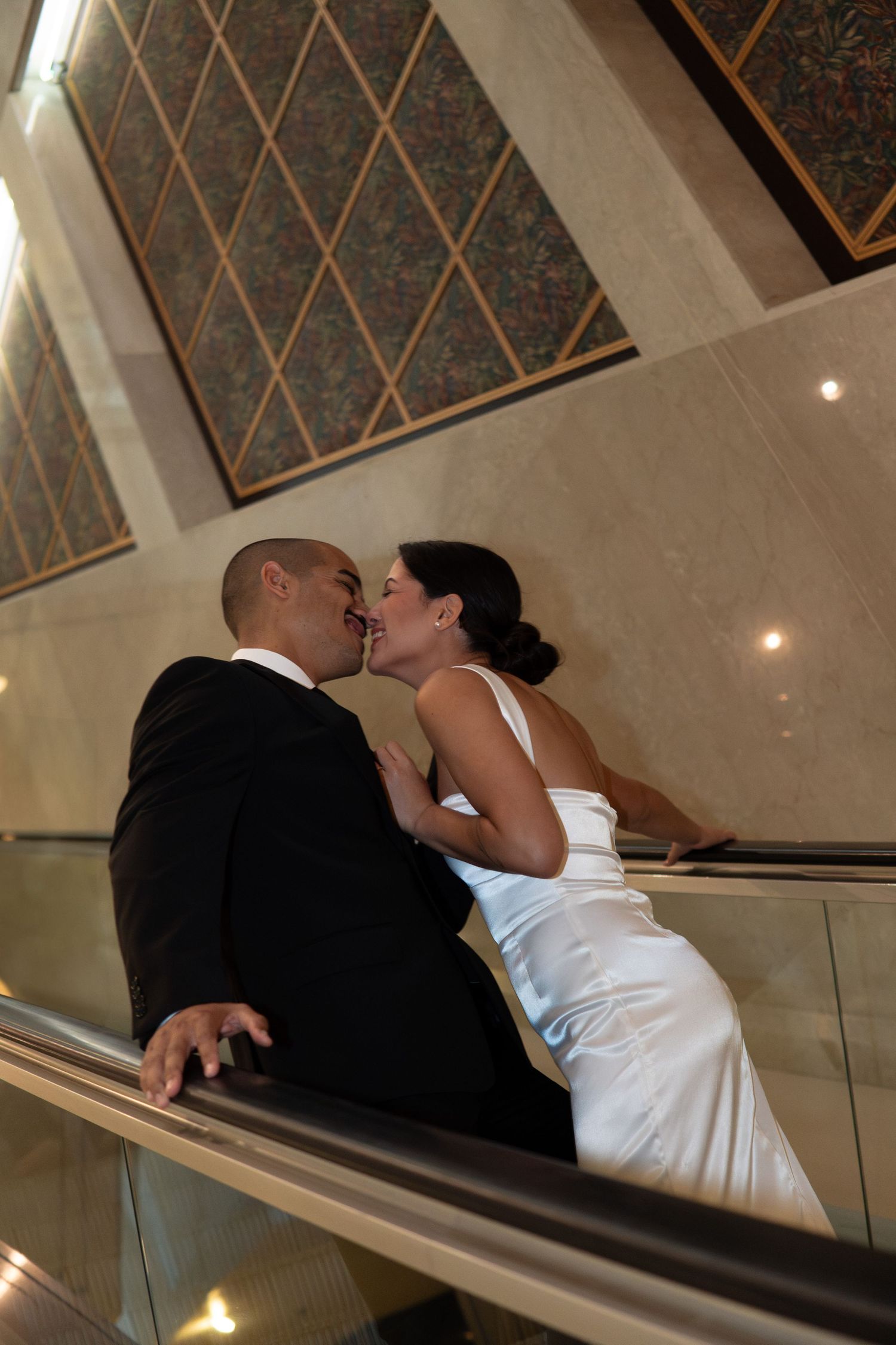 Bride and groom sharing a romantic kiss on an escalator, captured from a low angle perspective.