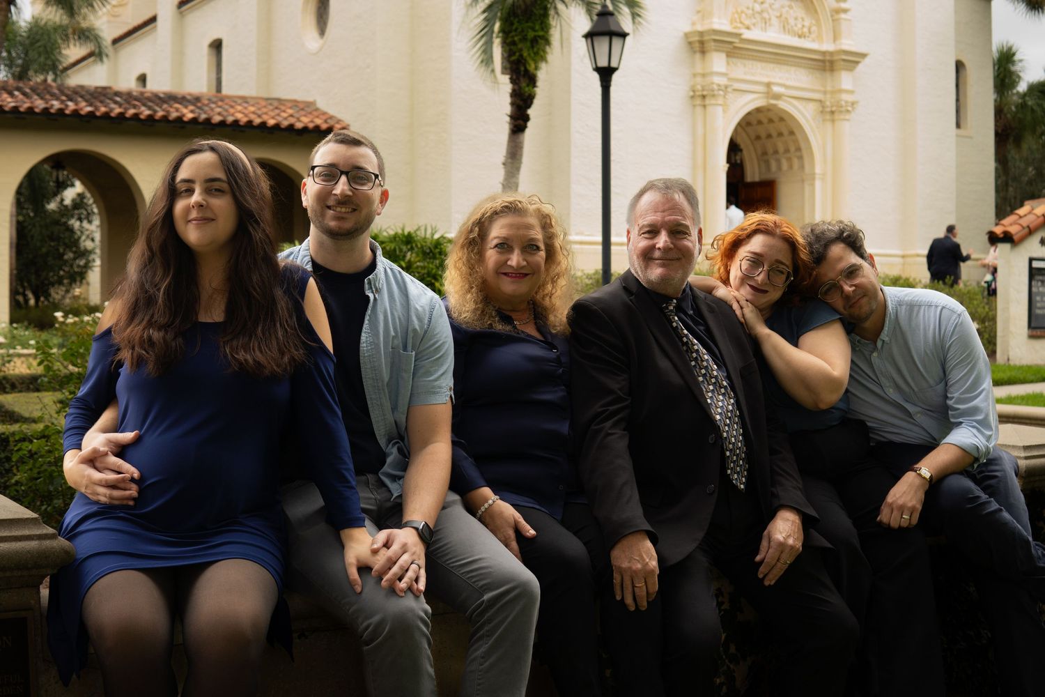 Group of six people smiling together outside a white Spanish-style building.