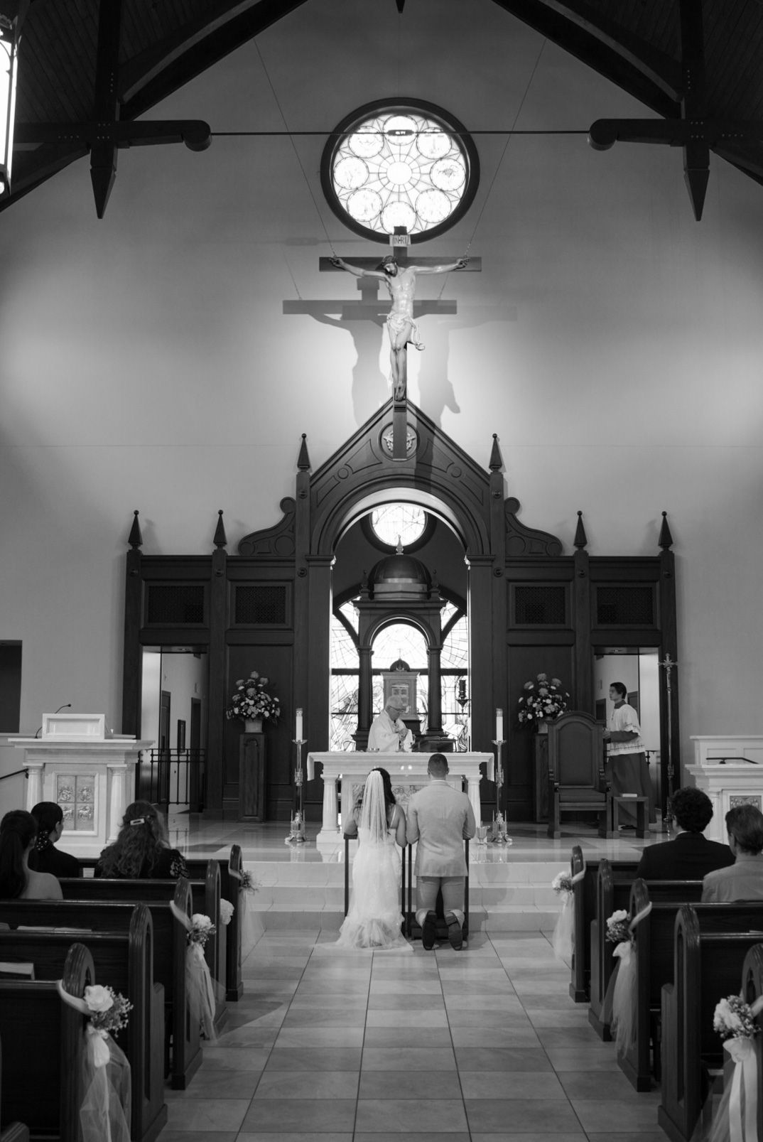 Black and white photo of bride and groom kneeling at altar in traditional Catholic church ceremony.